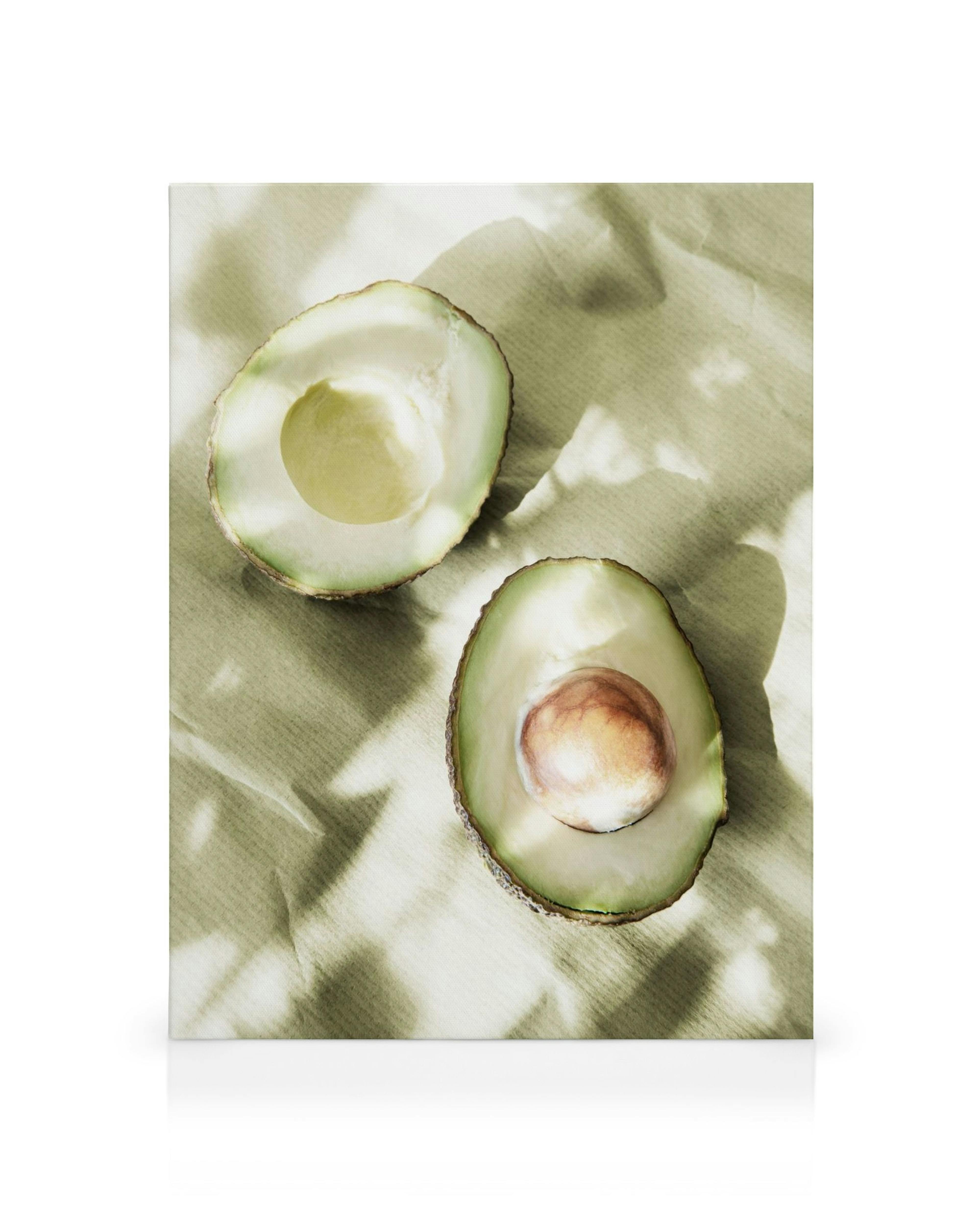Obraz na płótnie: dwie połówki awokado na jasnobeżowym tle, jedna z pestką, w słońcu. Sztuka kulinarna.