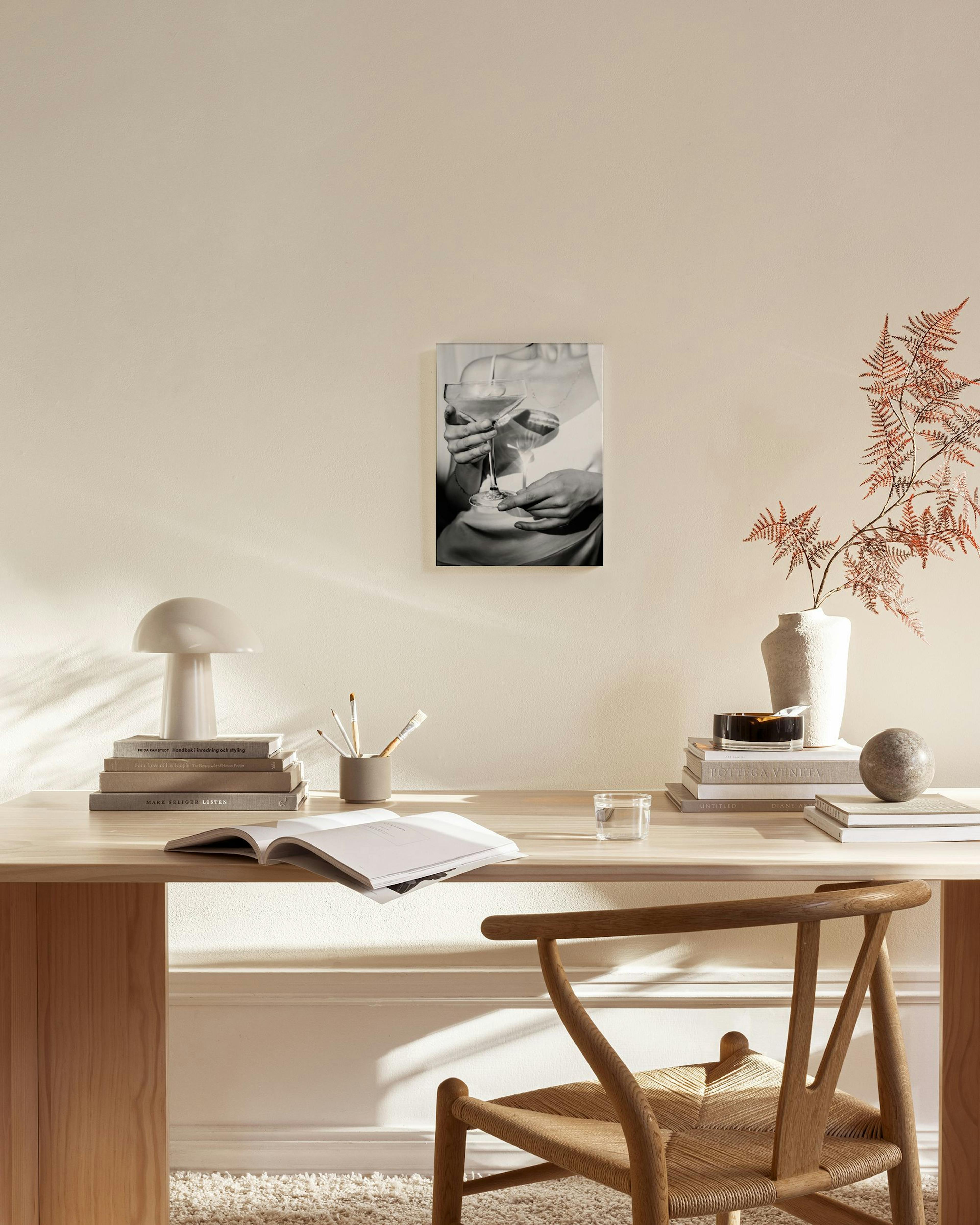 Tela decorativa a preto e branco de uma mulher a segurar um copo de cocktail, pendurada numa sala de estar minimalista.