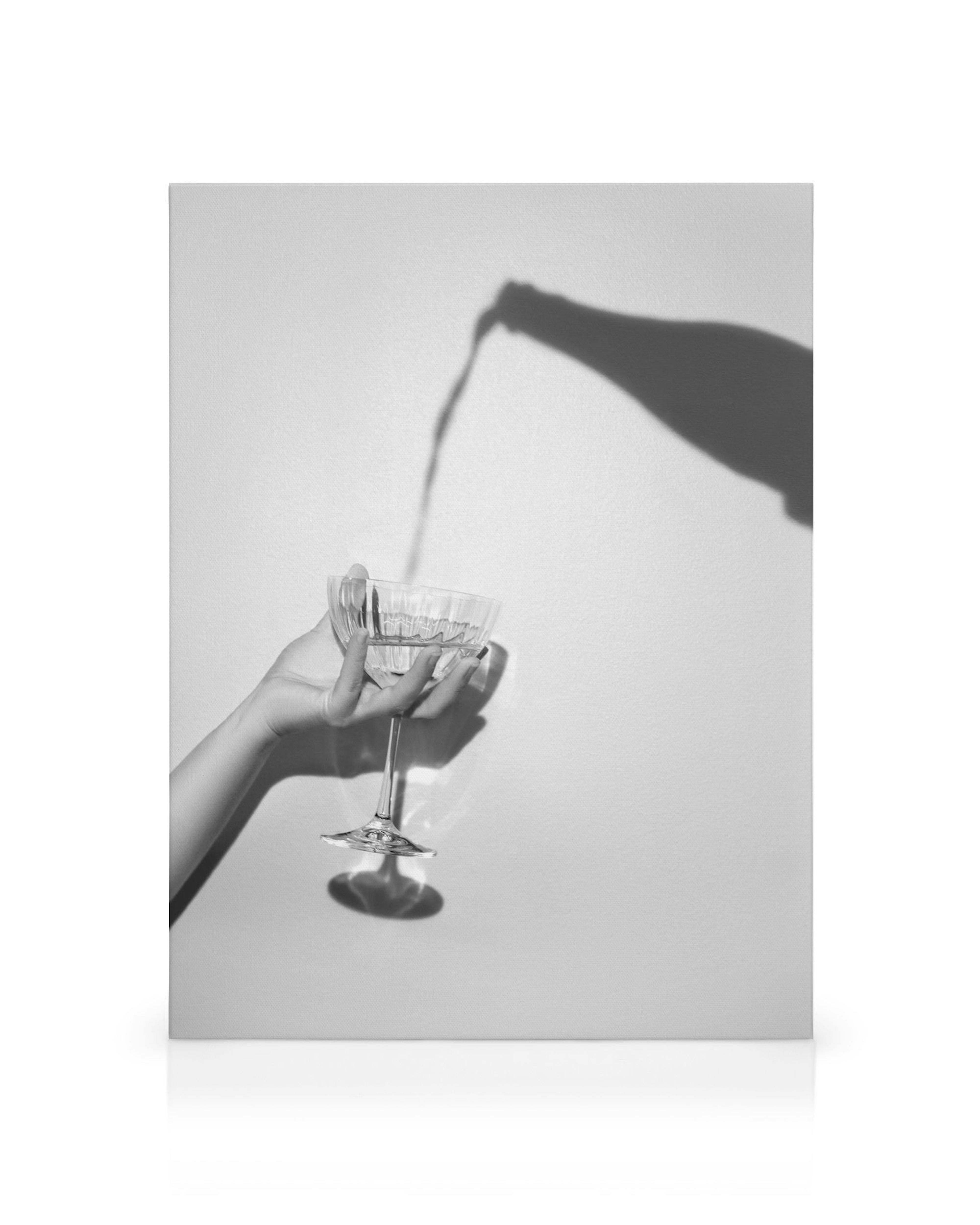 Svartvit canvastavla av en hand som håller ett glas, med en skugga av en flaska som häller en drink.