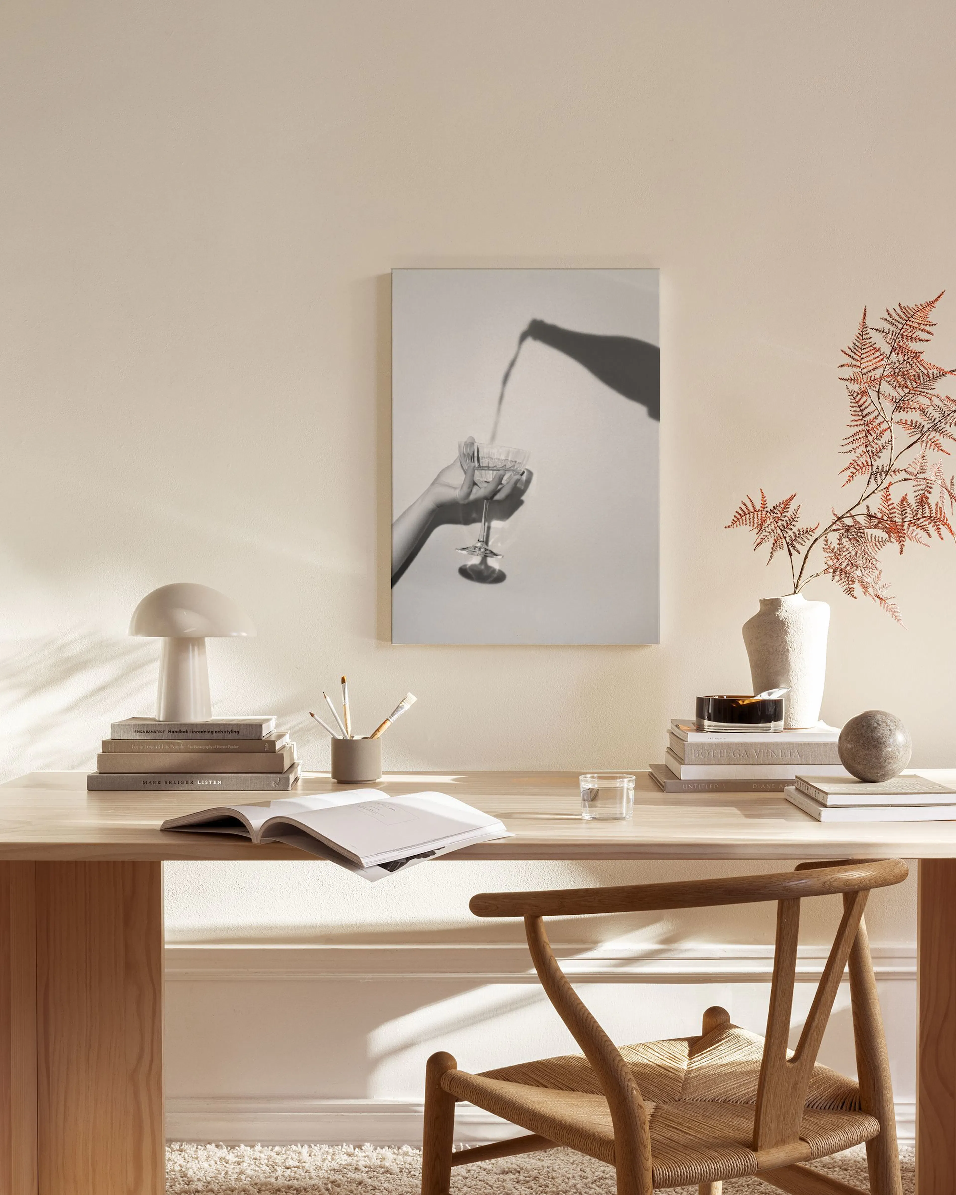 Schwarz-weiß Leinwandbild mit Hand, die Sekt in ein Glas gießt, hängend im stilvollen Wohnzimmer über einem Sideboard.