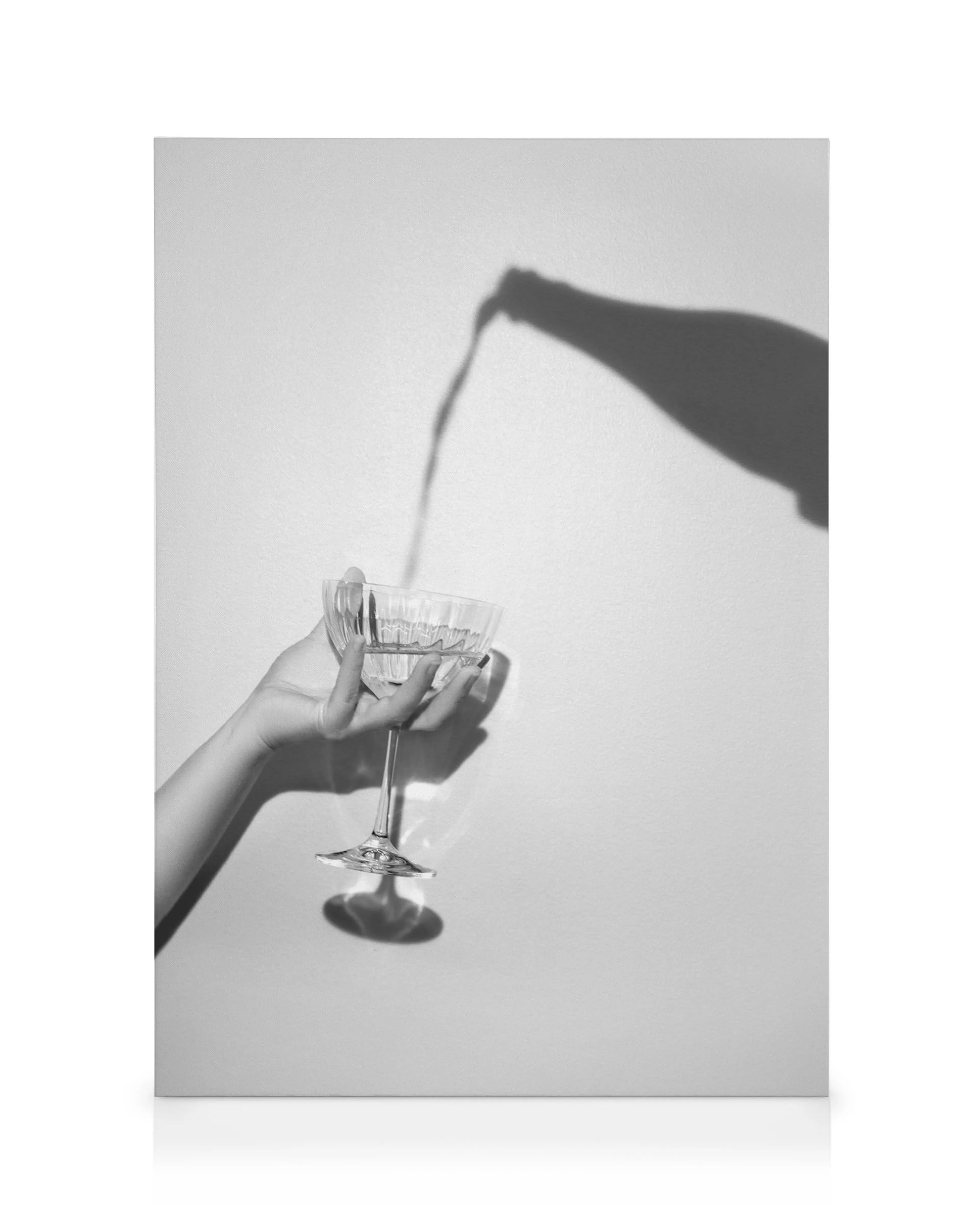 Schwarz-weißes Foto einer Hand, die ein Glas hält, in das Wein gegossen wird, mit Flaschenschatten.