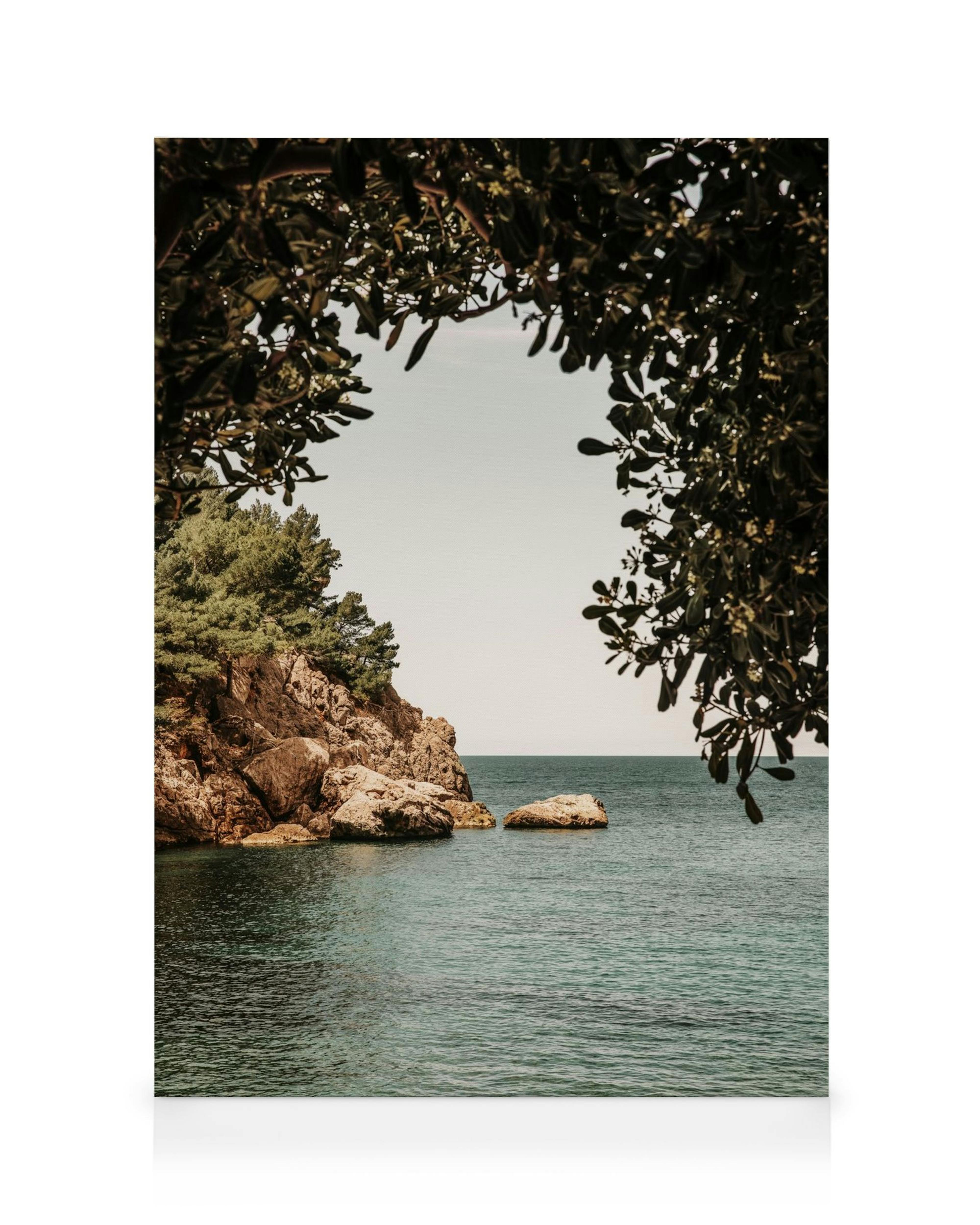 Leinwanddruck mit Blick auf das Meer durch einen natürlichen Bogen aus Blättern, Felsen und Bäumen an der Küste.