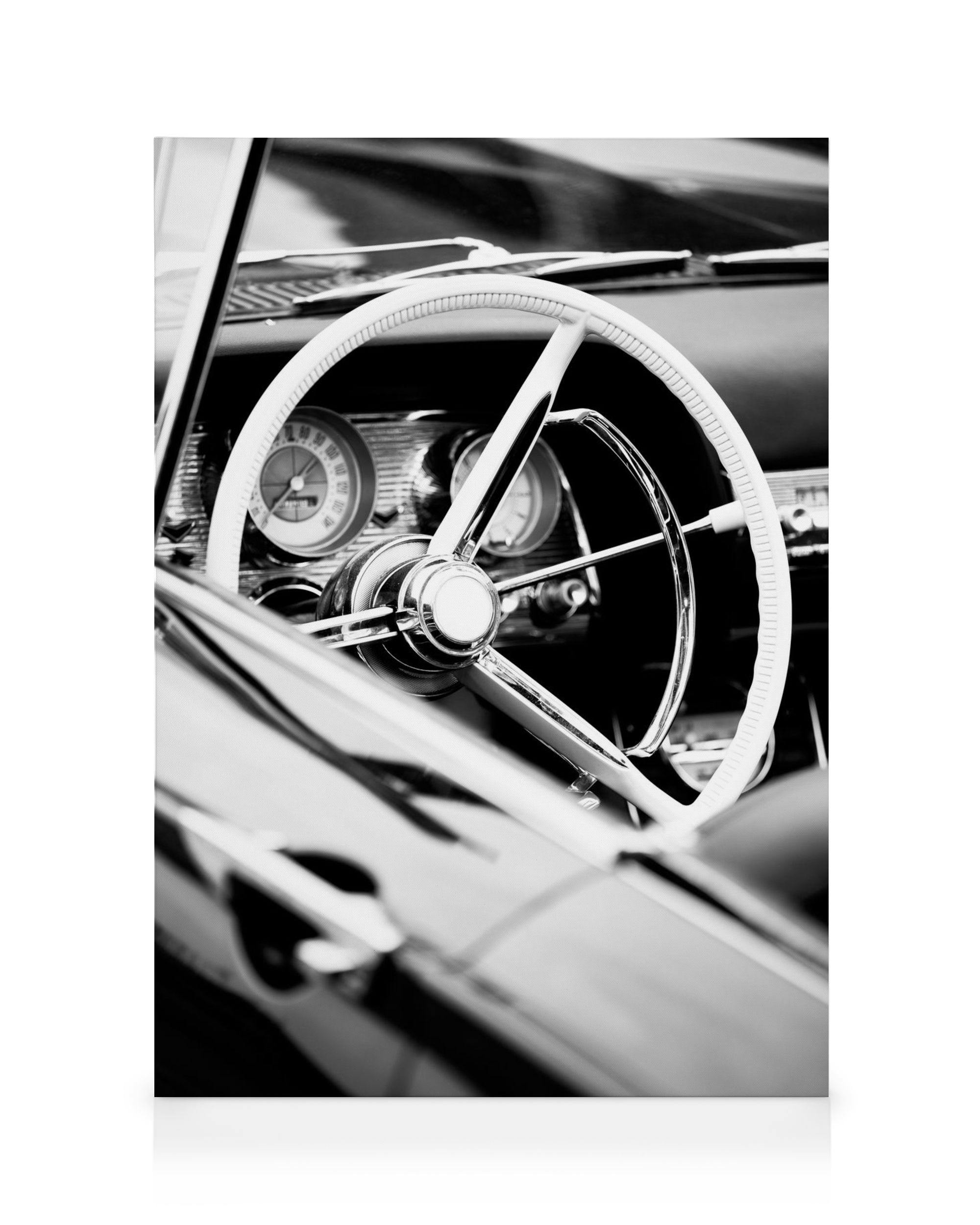 Mustavalkoinen kuva vintage-avoauton ohjaamosta, valkoinen ohjauspyörä ja mittaristo näkyvissä.