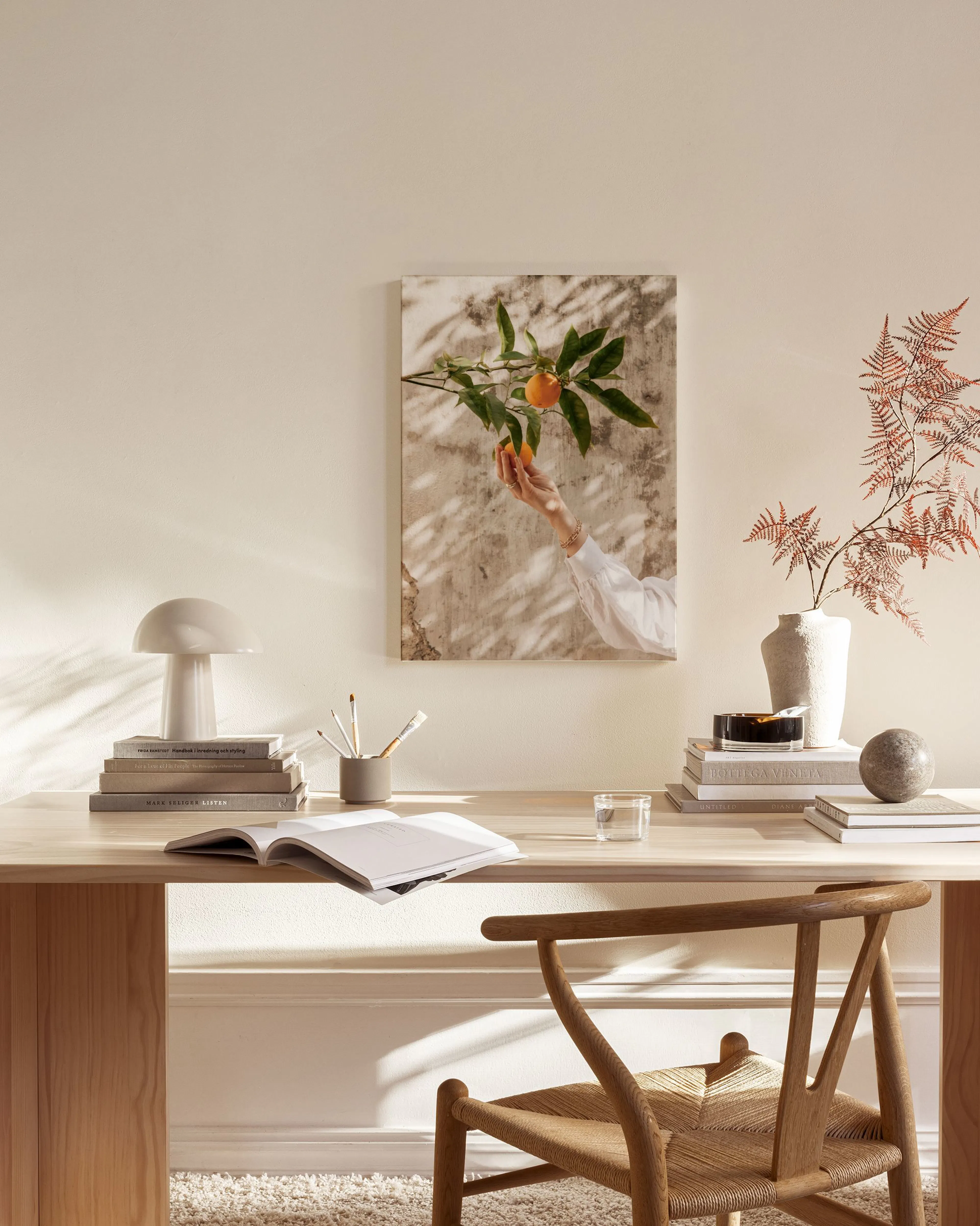 A canvas print of a hand reaching for oranges on a branch, hanging above a wooden console table in a minimalist living room.