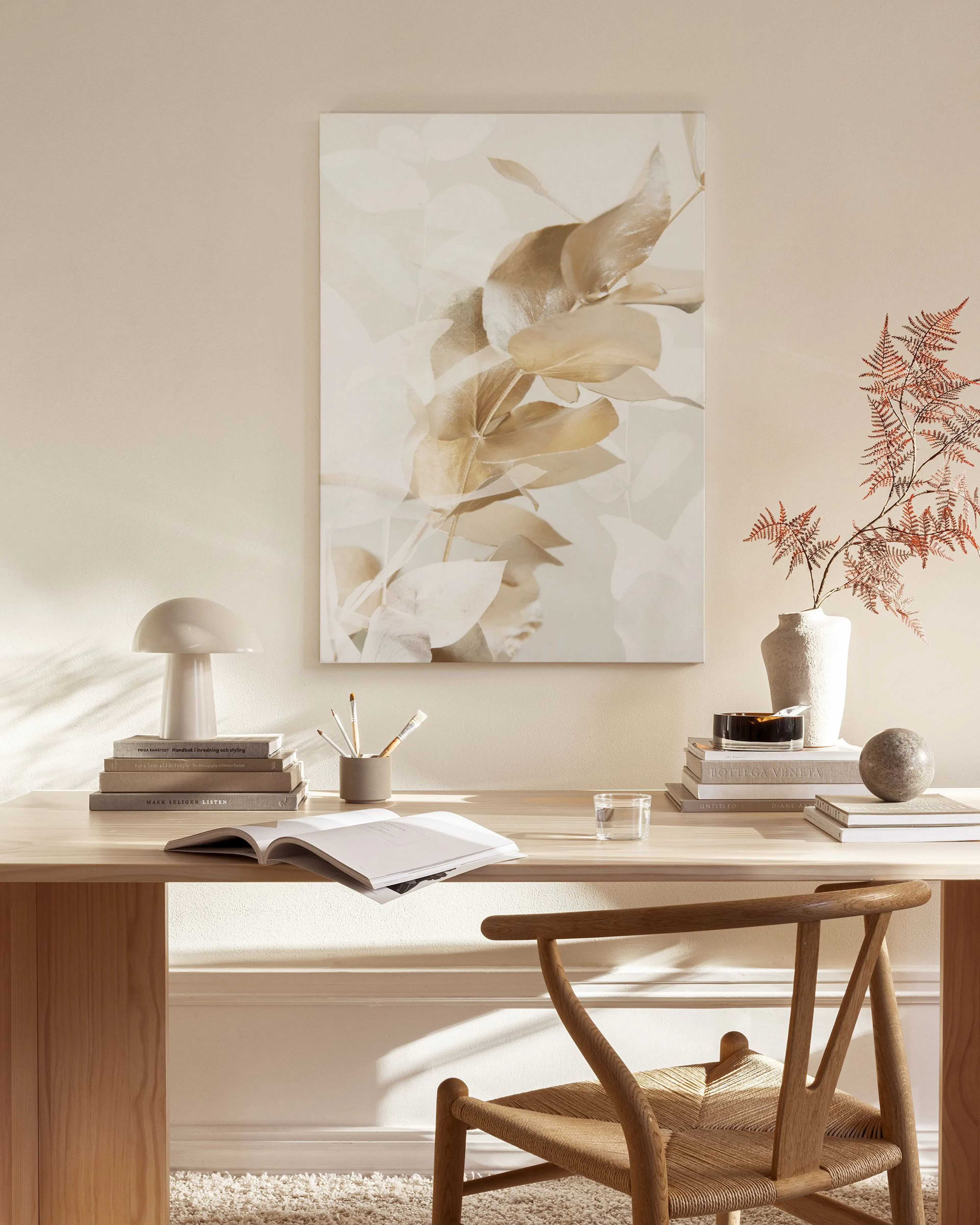 Botanical canvas print with warm beige and white leaves, displayed above a wooden console table in a minimalist living room.