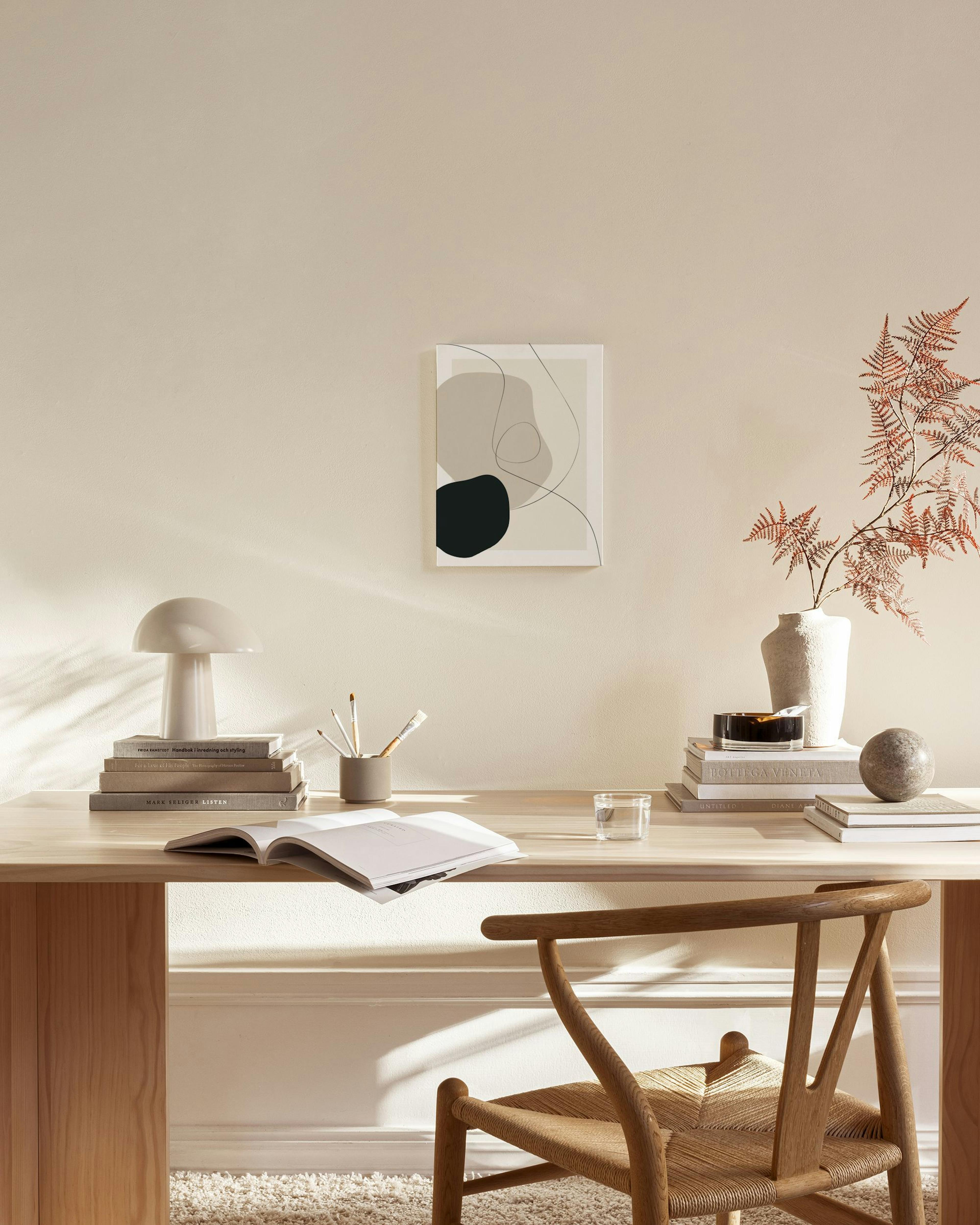 Et lærred med abstrakte former i sort, beige og grå og sorte linjer, der hænger i en lys stue.