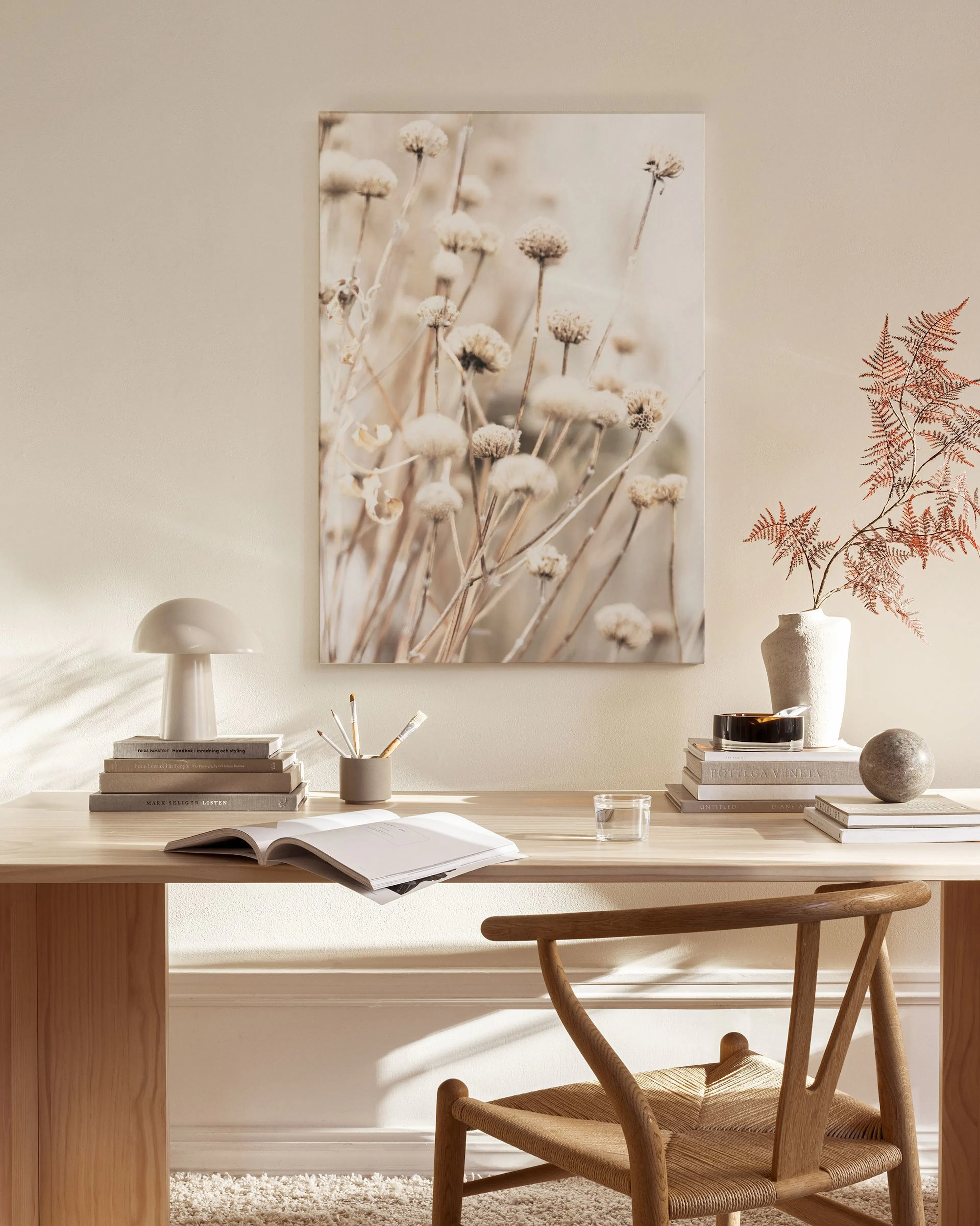 Canvas van droogbloemen in beige en bruintinten, hangend in een lichte, minimalistische woonkamer.
