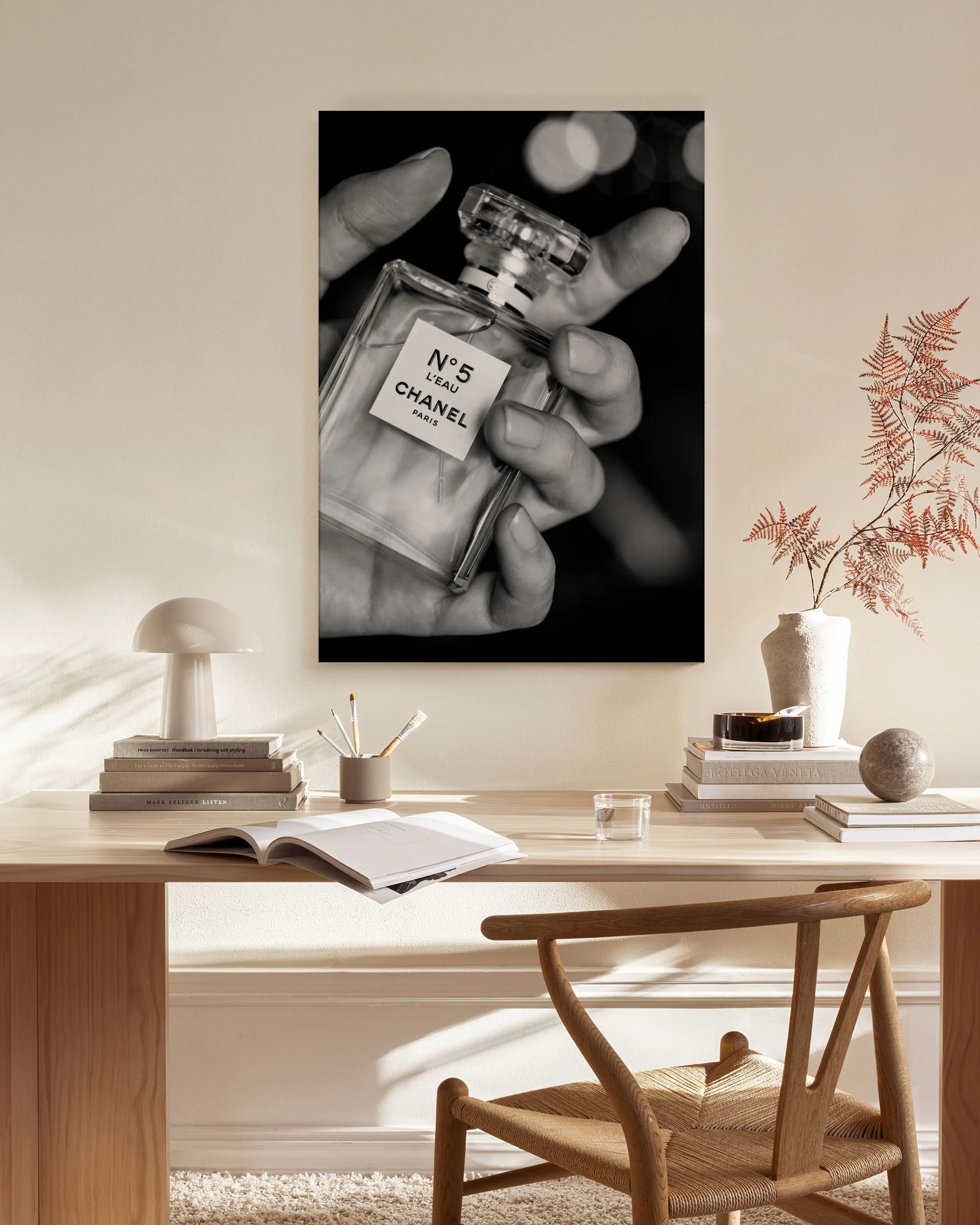 Sort/hvid lærred af en hånd, der holder en Chanel N°5 parfume, hængende i en stue over et træmøbel.