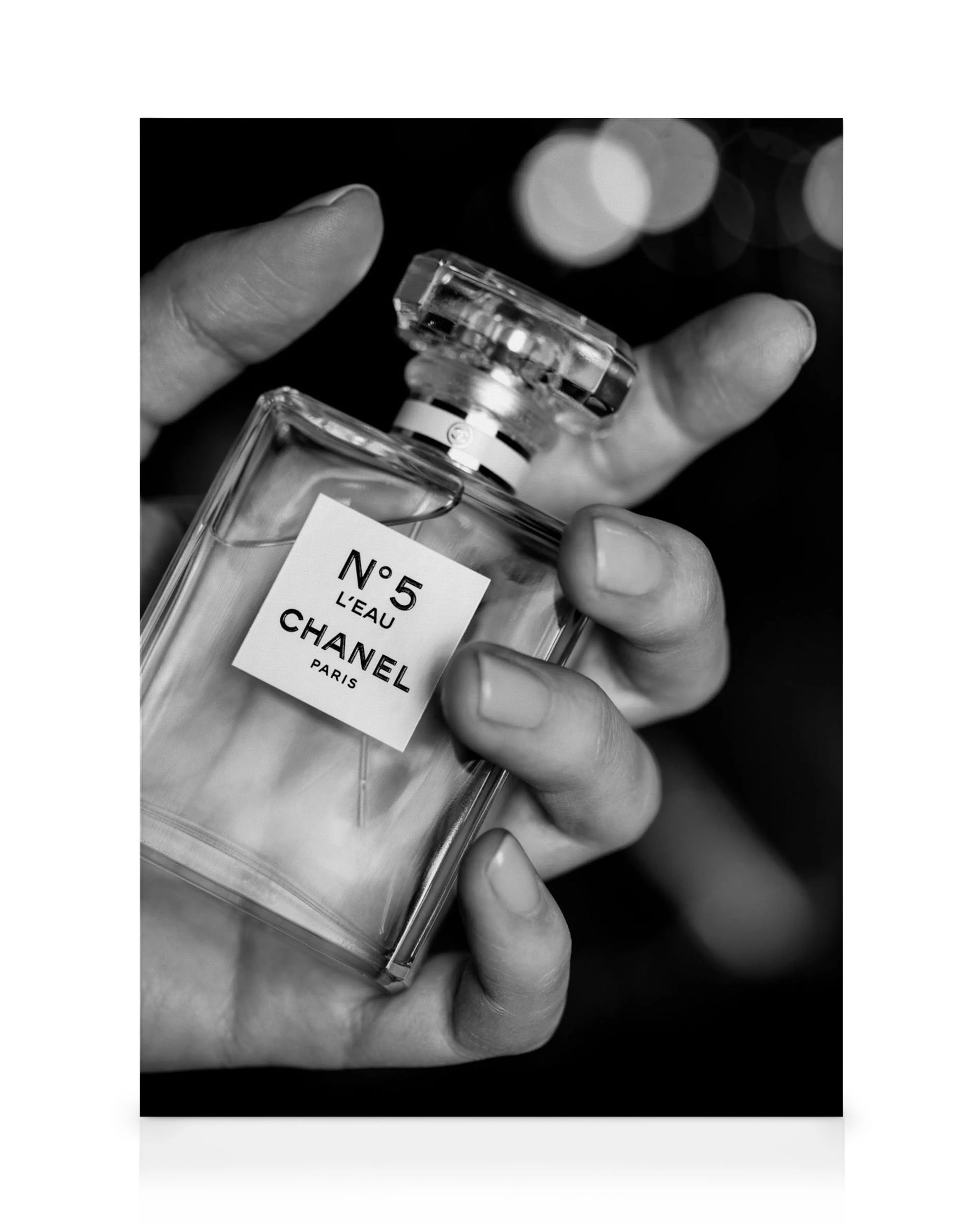Sorthvidt lærredstryk med en hånd, der holder en Chanel No5 parfume, detaljeret med logo og tekst.