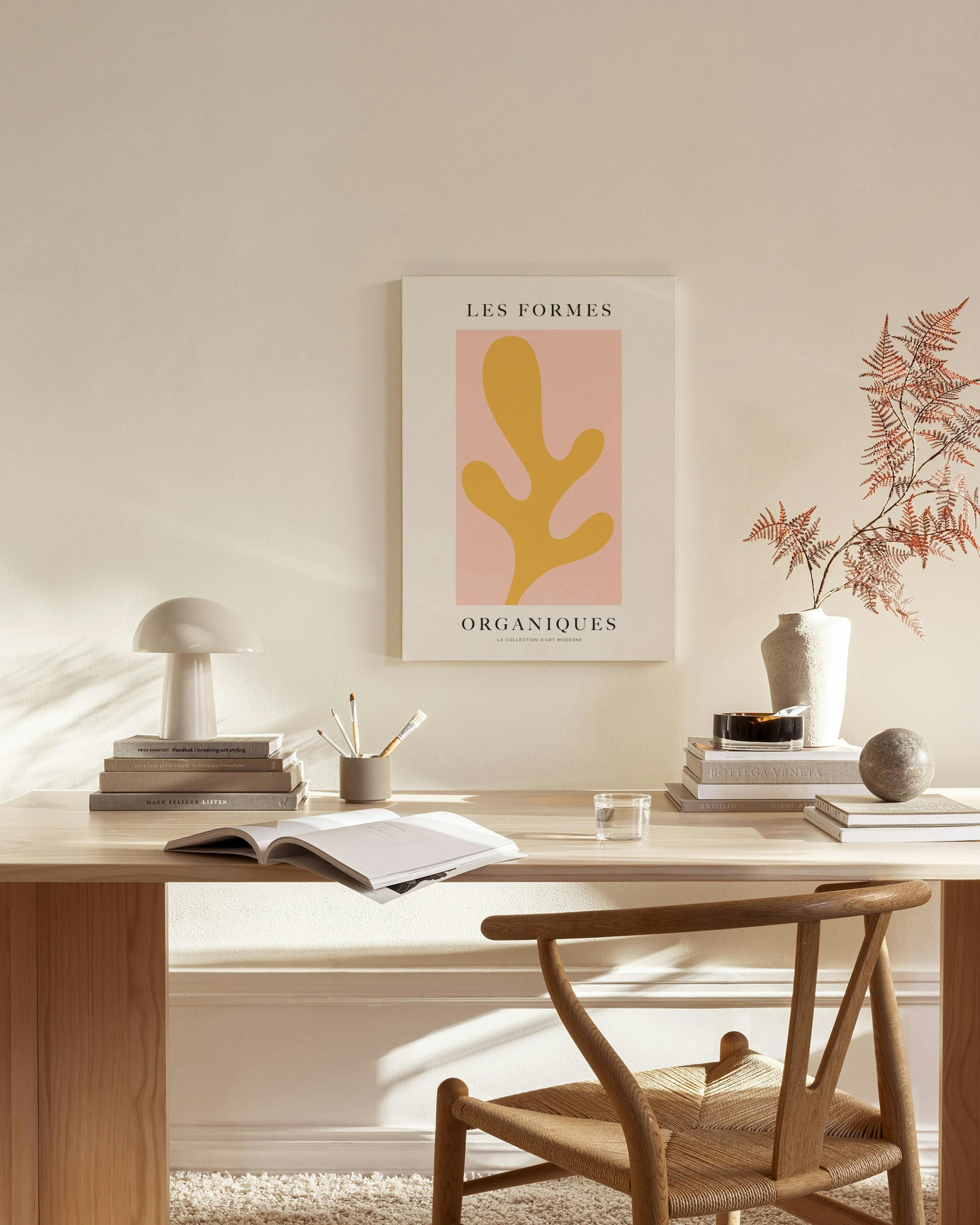 A canvas print with a yellow organic shape on a pink background, above a console table in a minimalist living room.