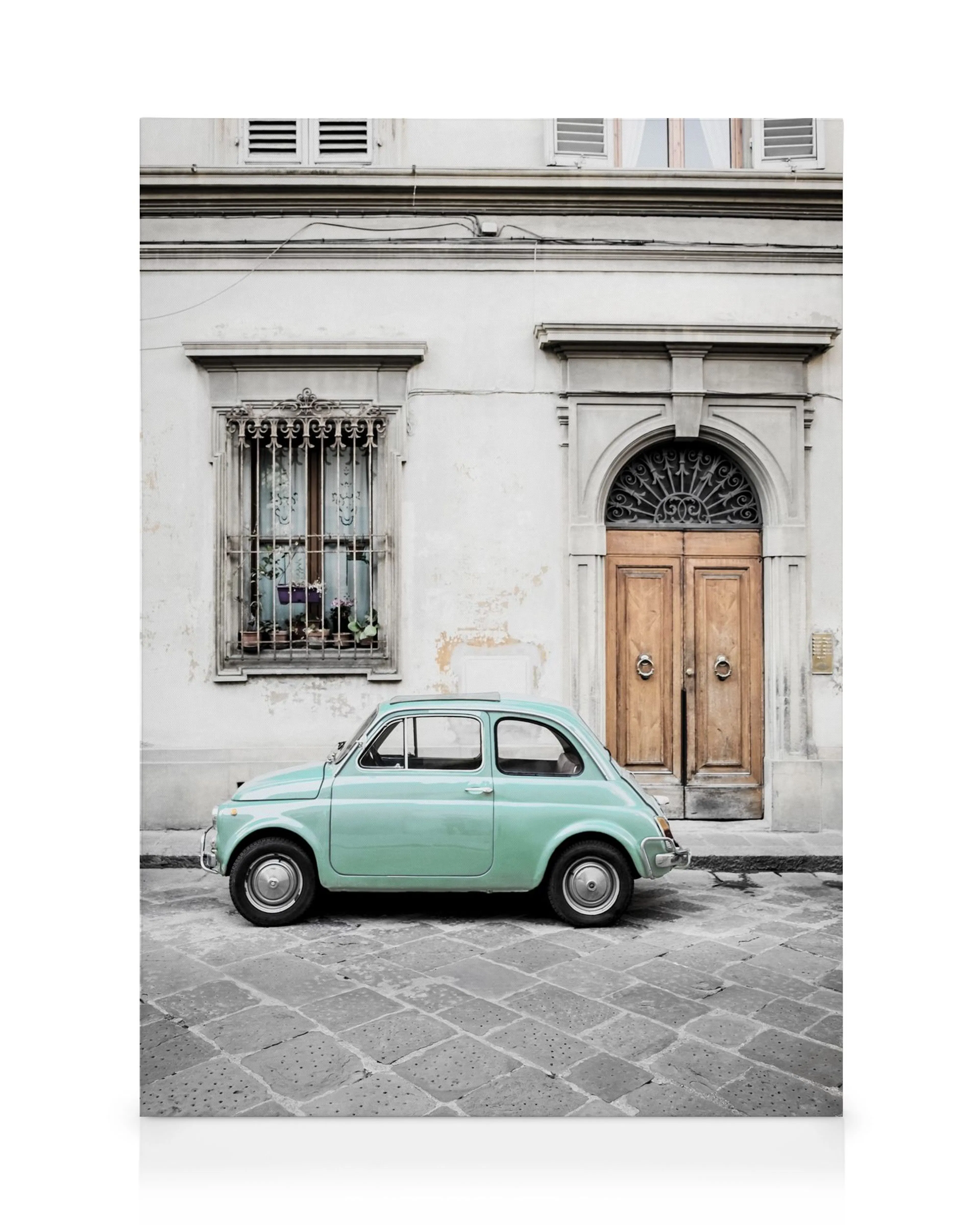 Vintage mintgroene Fiat 500 geparkeerd op Italiaanse kasseien voor een oud gebouw met houten deuren.