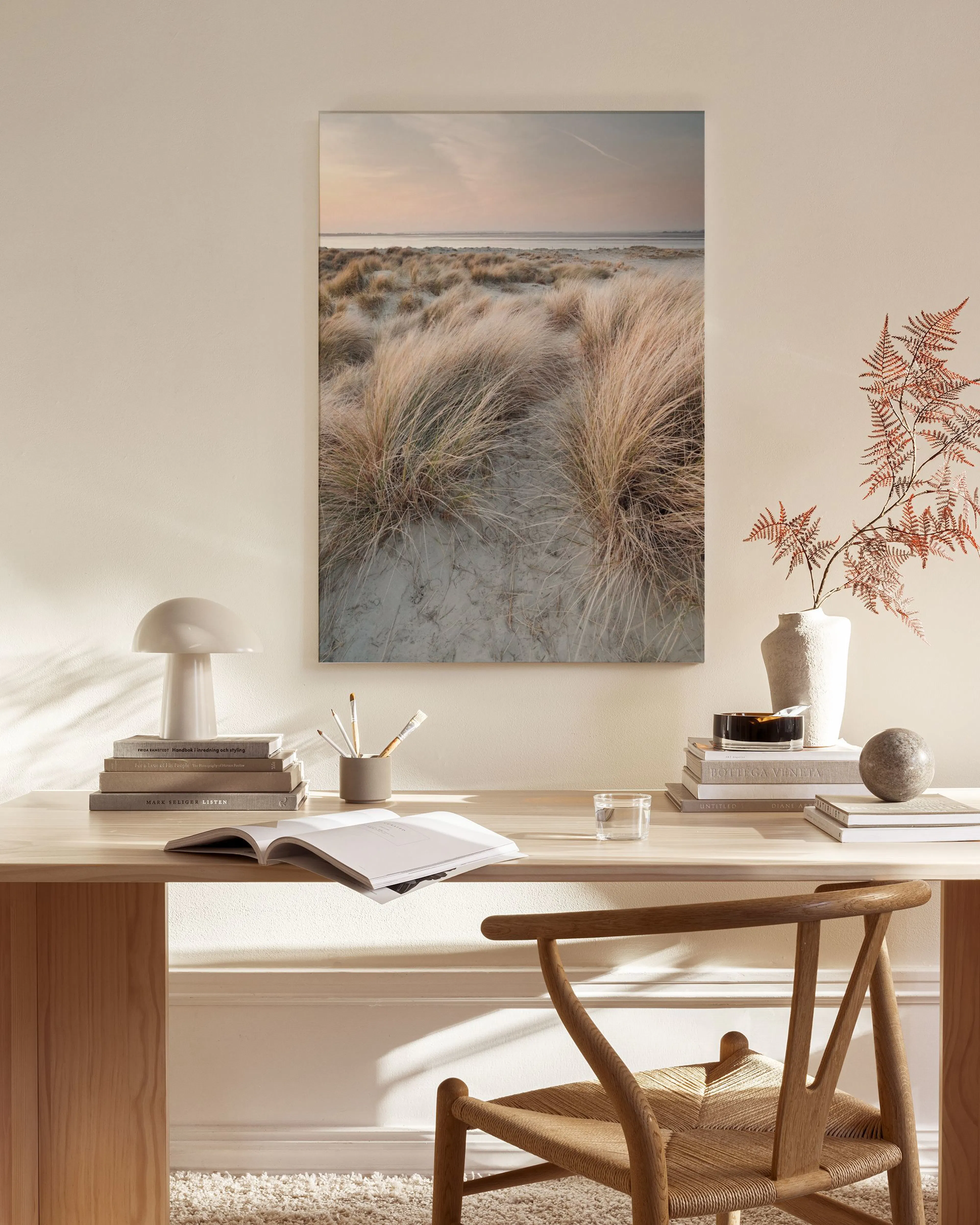 A canvas print of dry dune grass on a sandy beach with the ocean in the distance, hanging in a neutral modern living room.