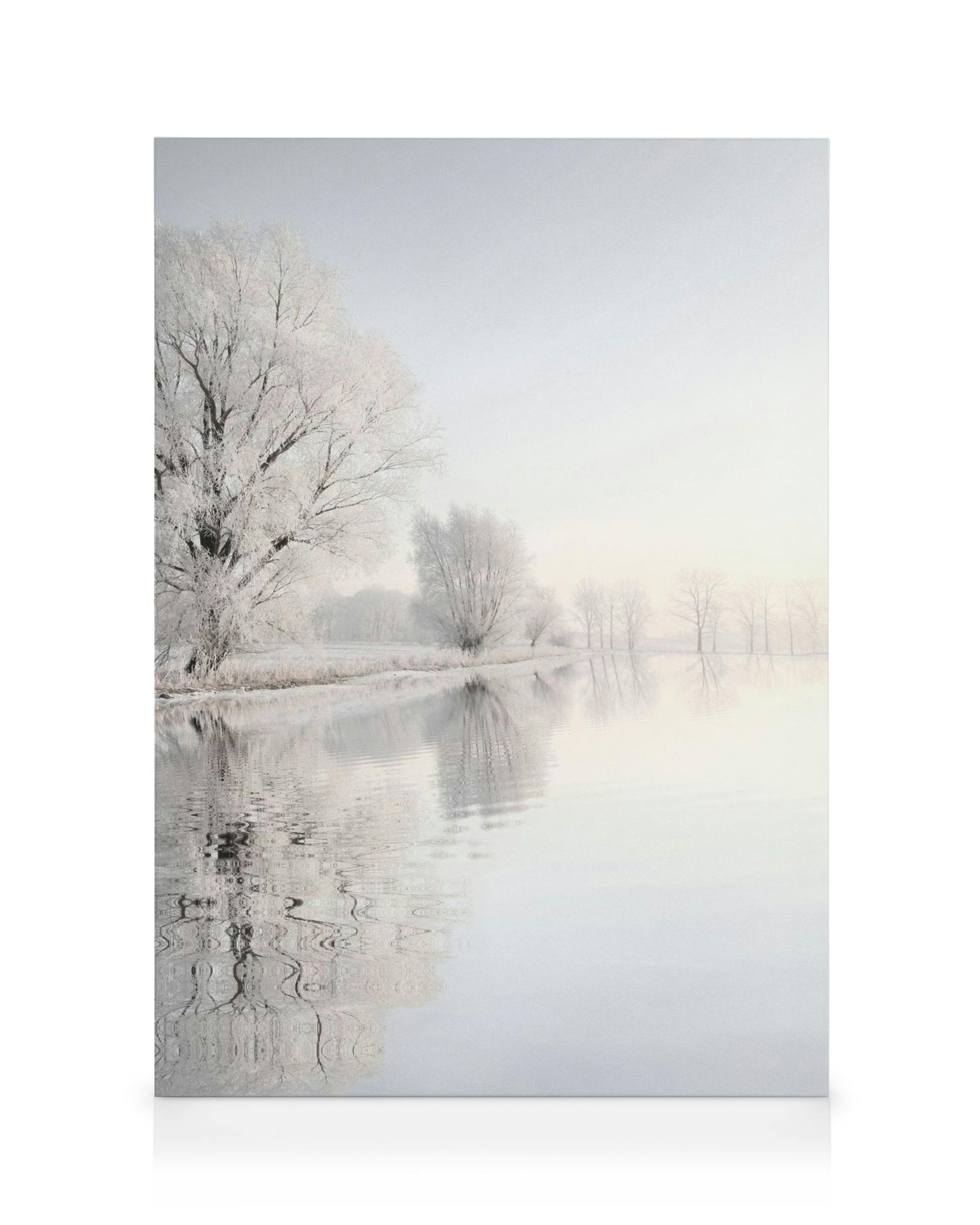 Canvastavla med frostigt vinterlandskap, träd som speglas i dimmigt vatten, i vita och gråblå nyanser.