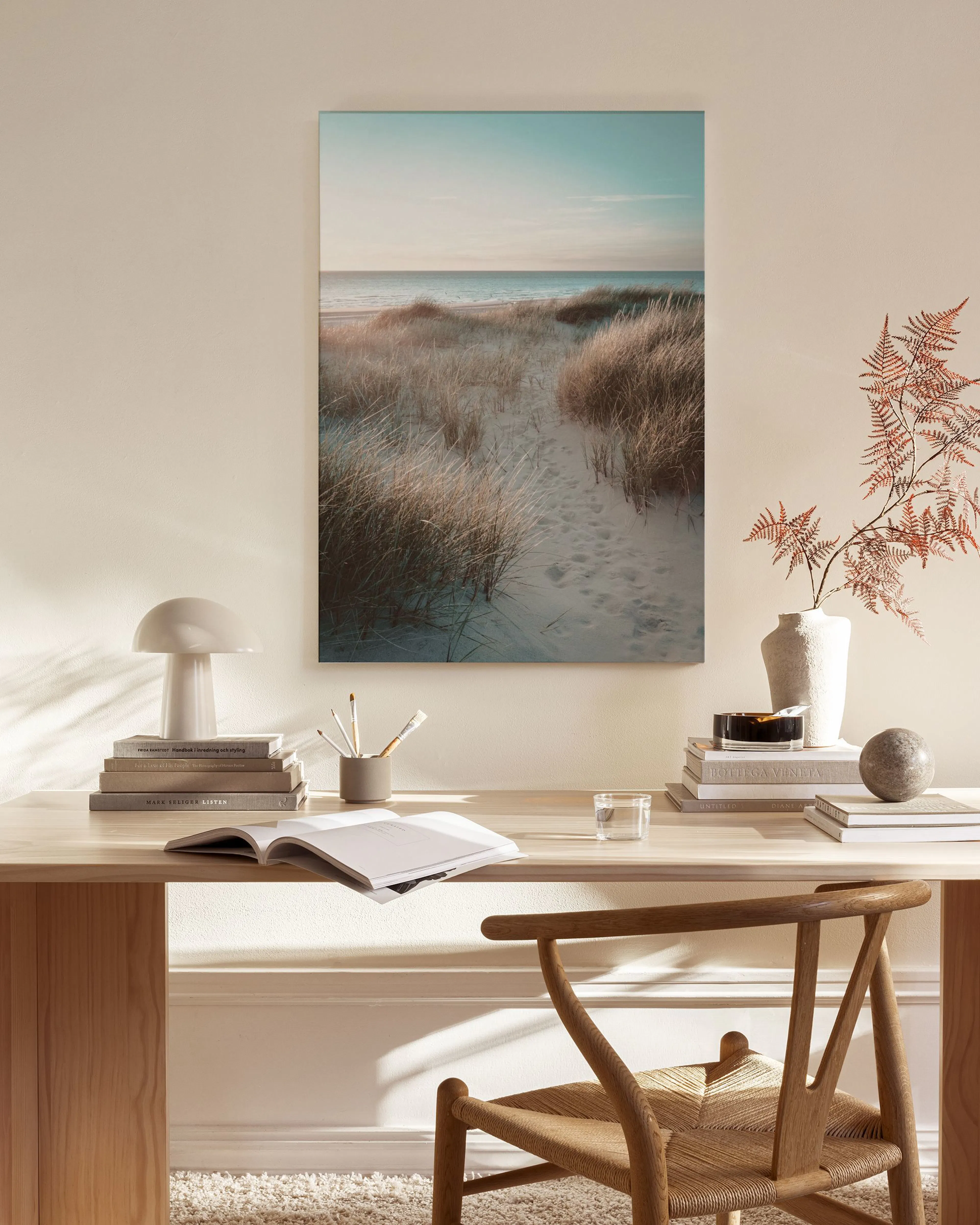 A canvas print of a sandy beach path through dunes to a calm sea, hanging in a bright, modern living room.