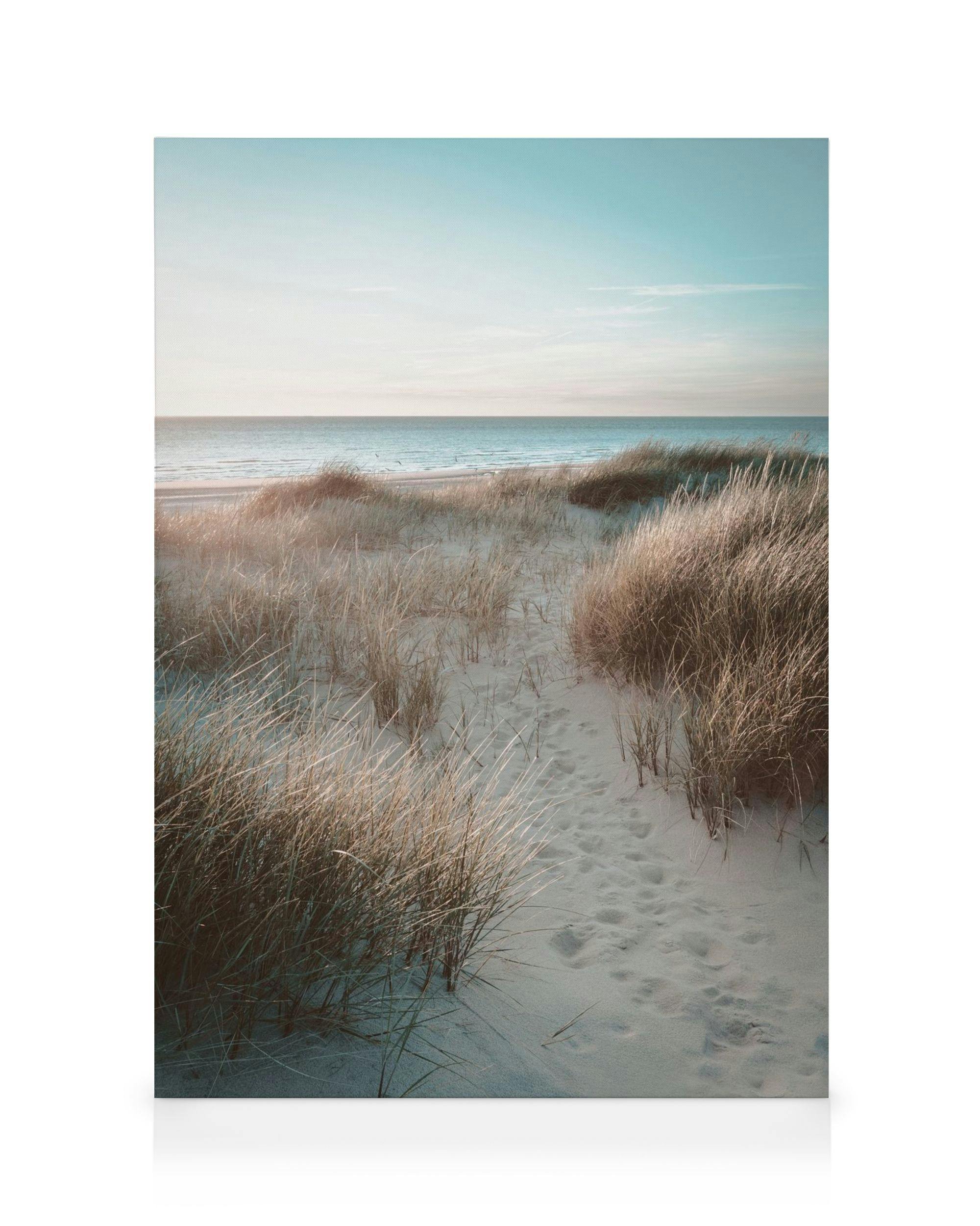 Toile de plage avec dunes de sable et empreintes menant à leau turquoise sous un ciel bleu nuageux