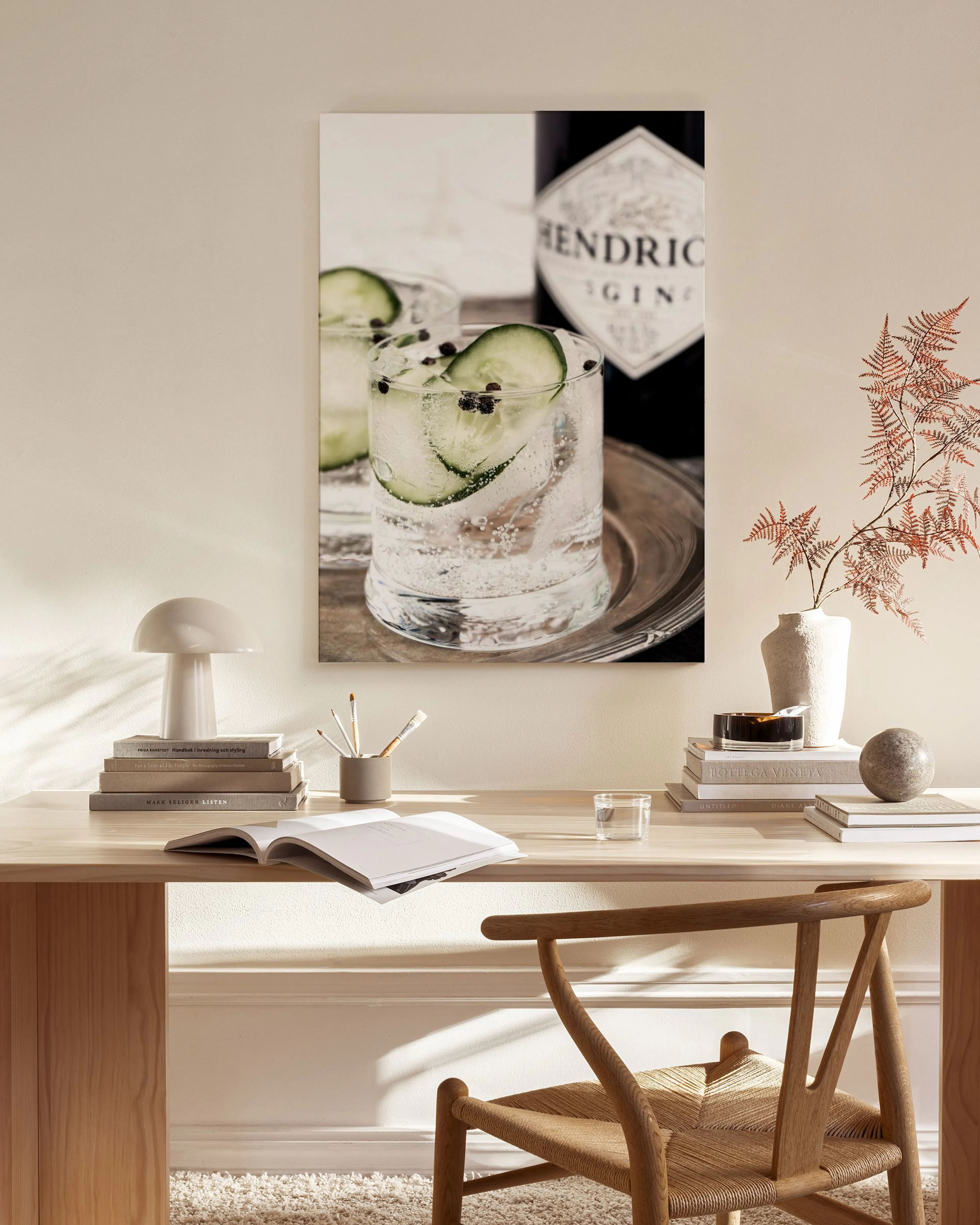 A canvas print of a gin and tonic cocktail with cucumber slices, displayed above a wooden console table in a minimalist living r