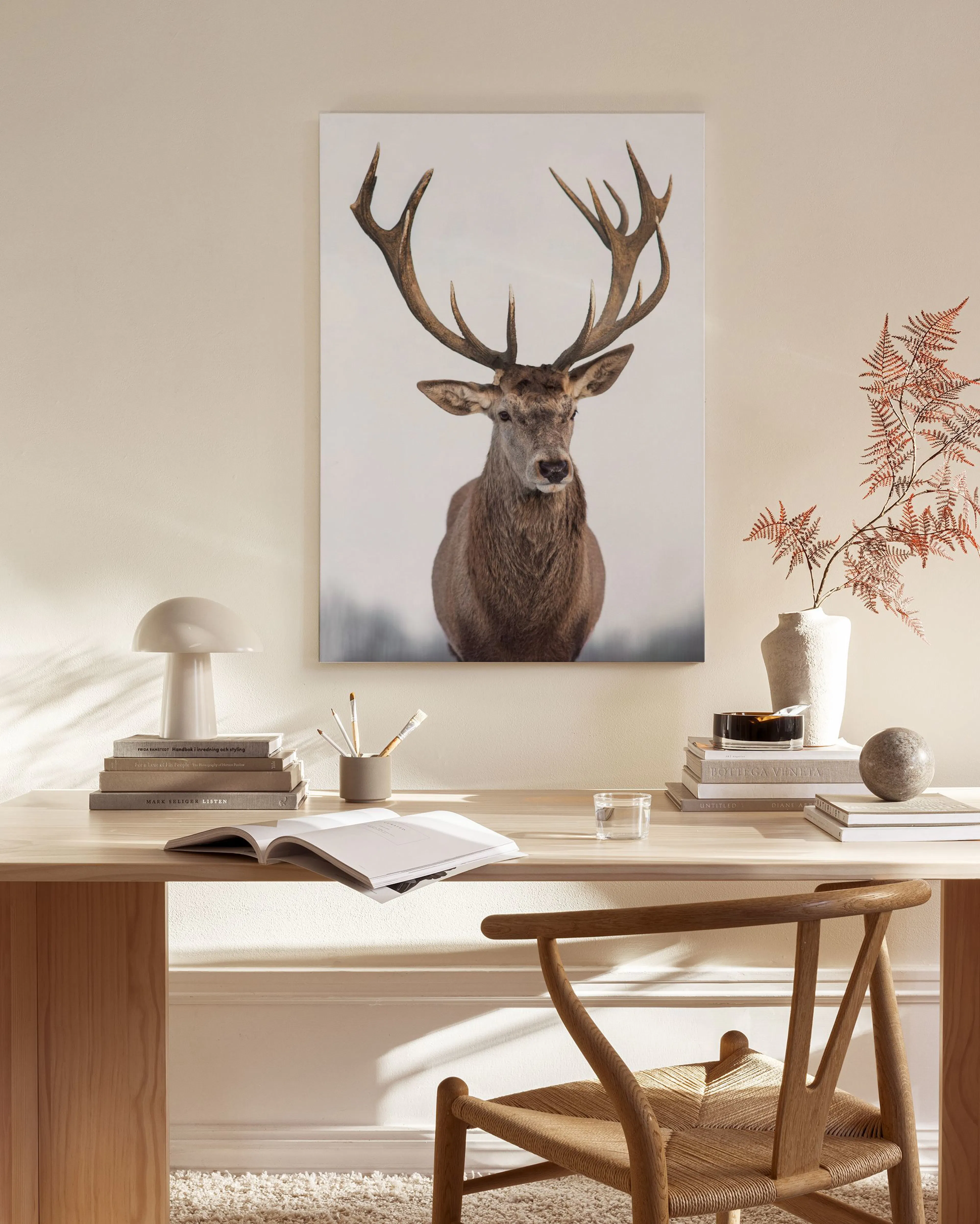 Canvas van een hert met groot gewei, hangend boven een houten dressoir in een lichte woonkamer.