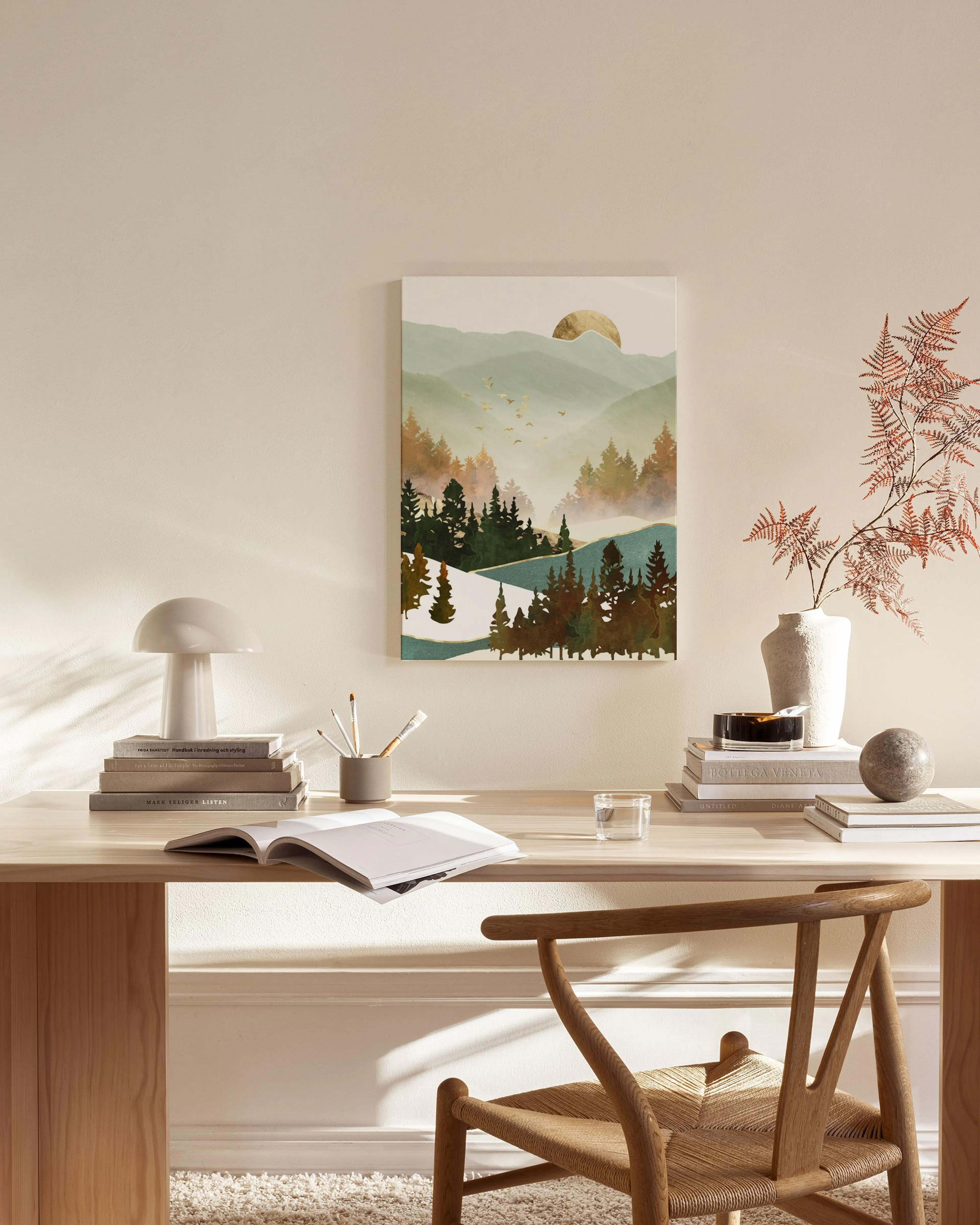 Tela decorativa de paisagem montanhosa com pinheiros e nuvens, com um sol dourado e revoada de pássaros, pendurada numa sala de 