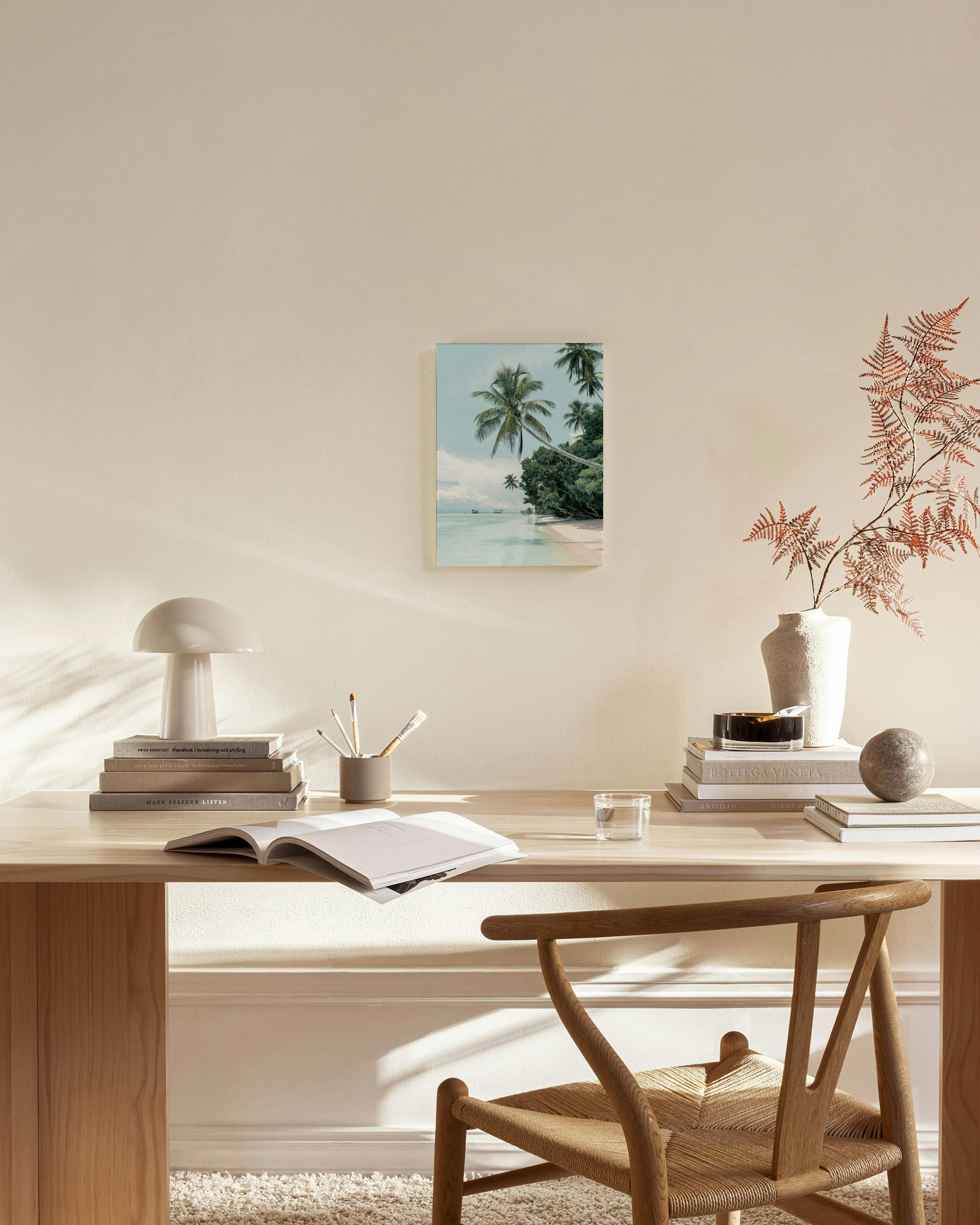 Leinwandbild mit Palmenstrand, türkisfarbenem Meer und weißem Sand, hängend in einem hellen Wohnzimmer über einer Holzbank.