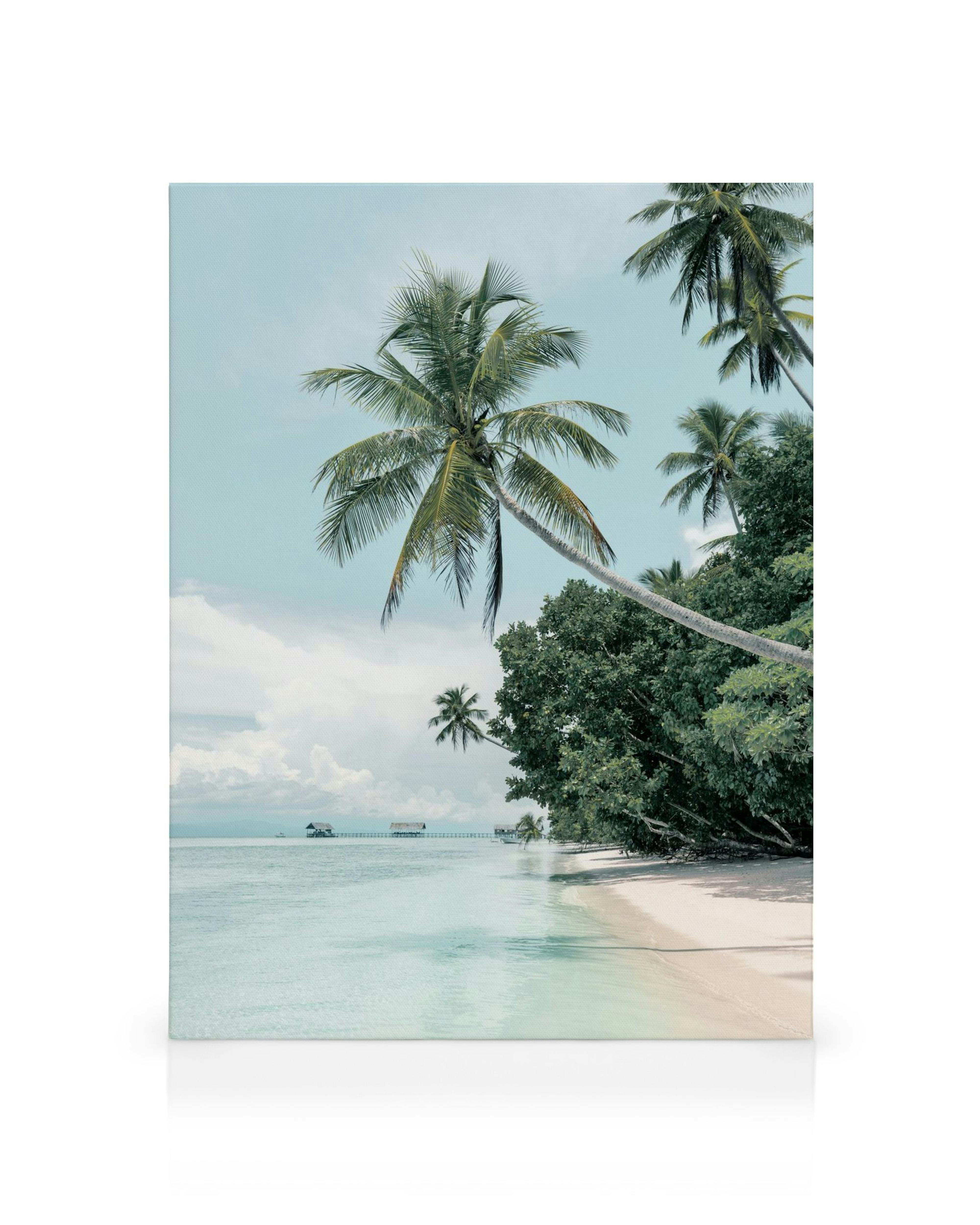 Leinwandbild tropischer Sandstrand mit Palmen, türkisblauem Meer und Stelzenhäusern im Hintergrund