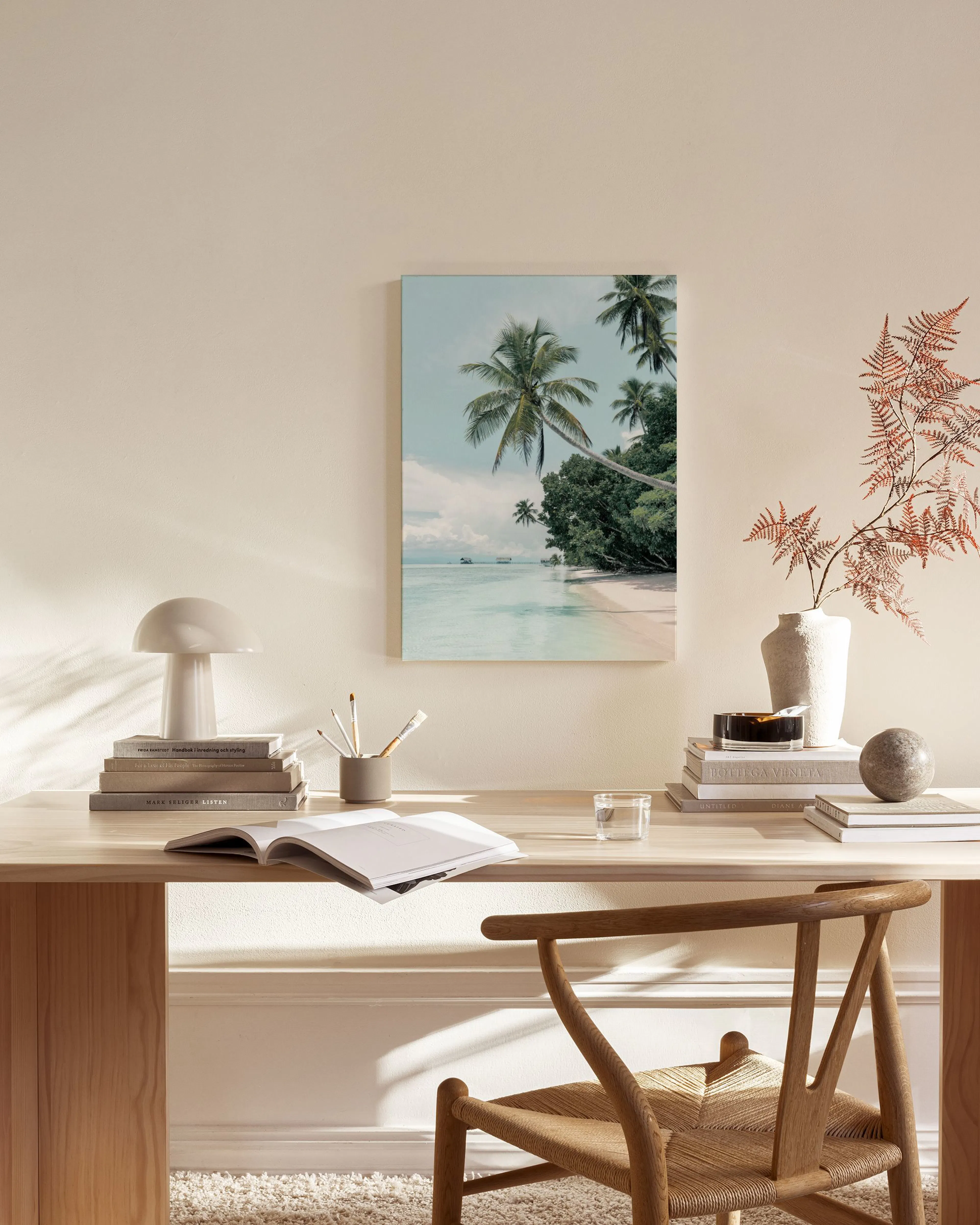 A tropical beach canvas print with palm trees and turquoise water, displayed in a minimal living room above a wooden console.