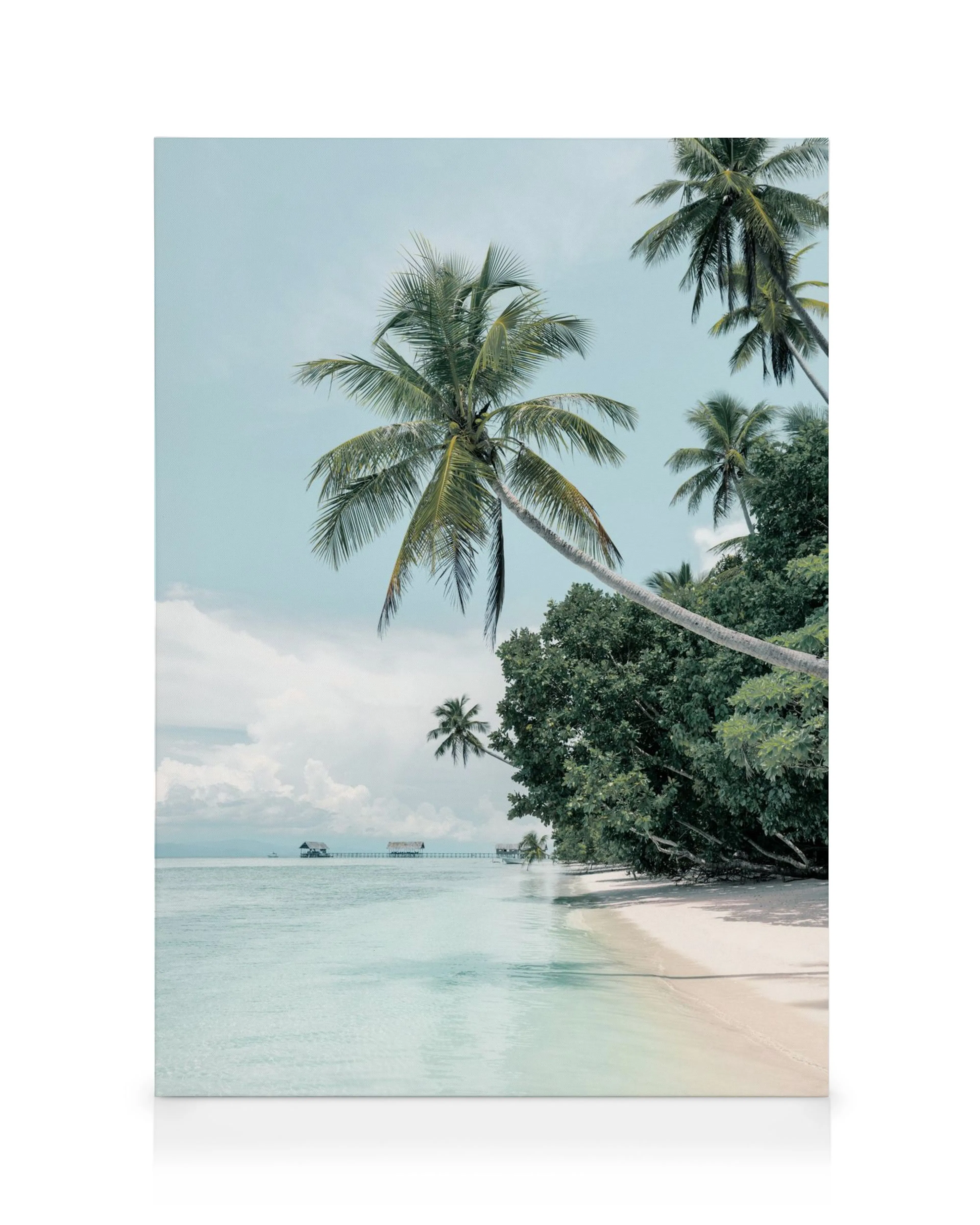 Tropical sand beach scene with palm trees, clear turquoise water, and distant overwater bungalows under a soft blue sky.