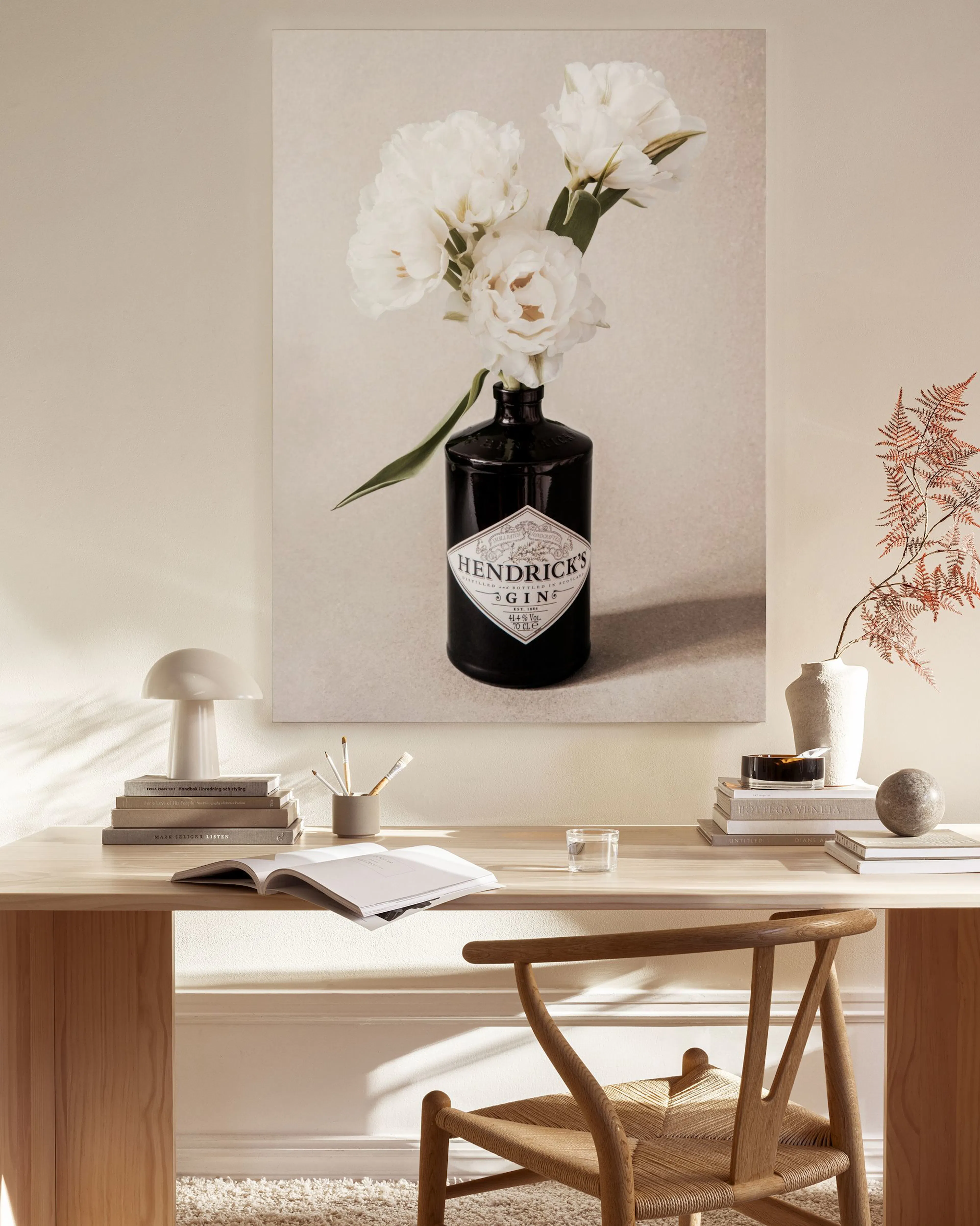 Toile dune bouteille de gin Hendricks avec des fleurs blanches, accrochée dans un salon lumineux au-dessus dun meuble bas en boi