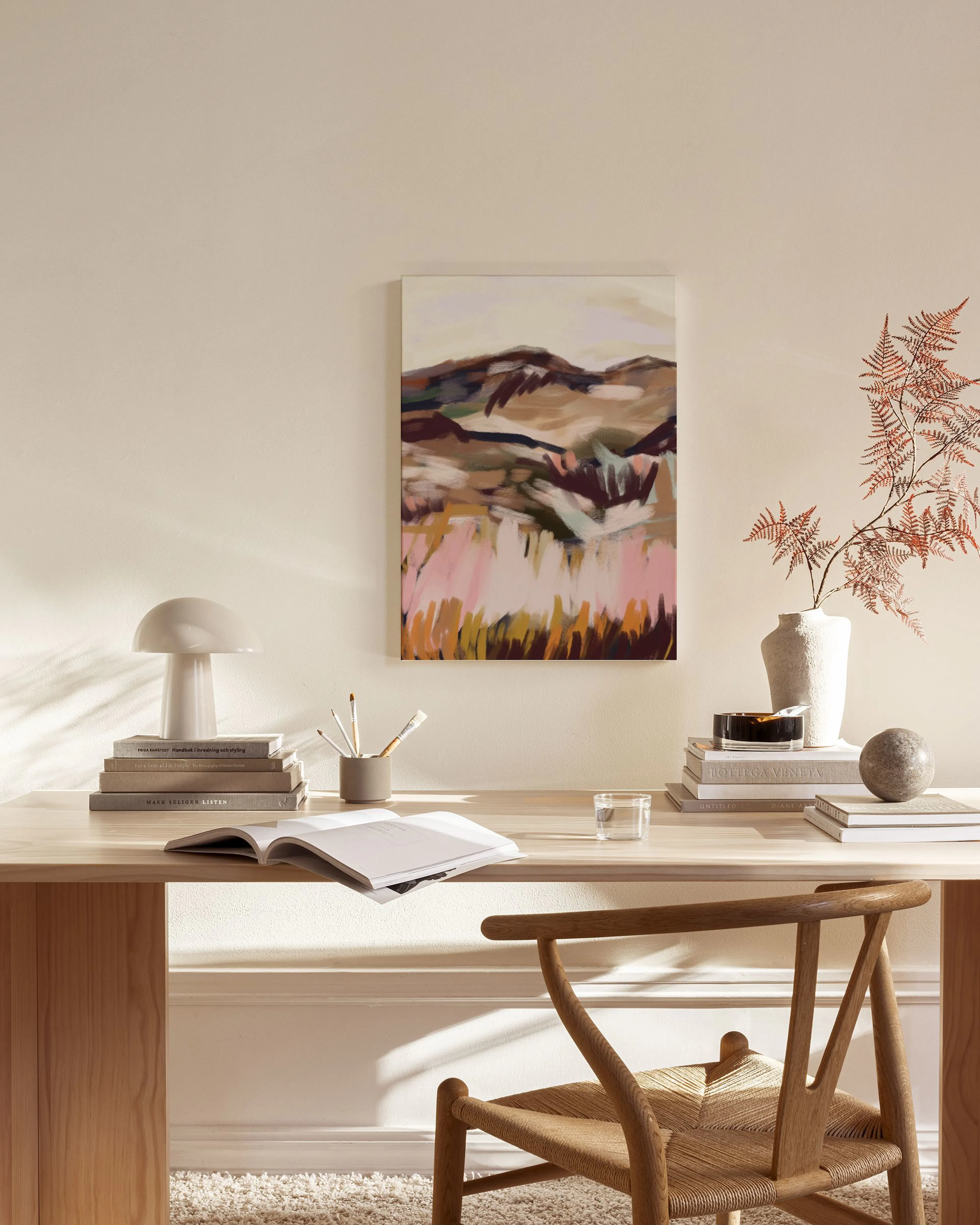 Canvas met roze, oranje en bruine landschapsvormen, hangend in een neutrale woonkamer boven een houten dressoir.