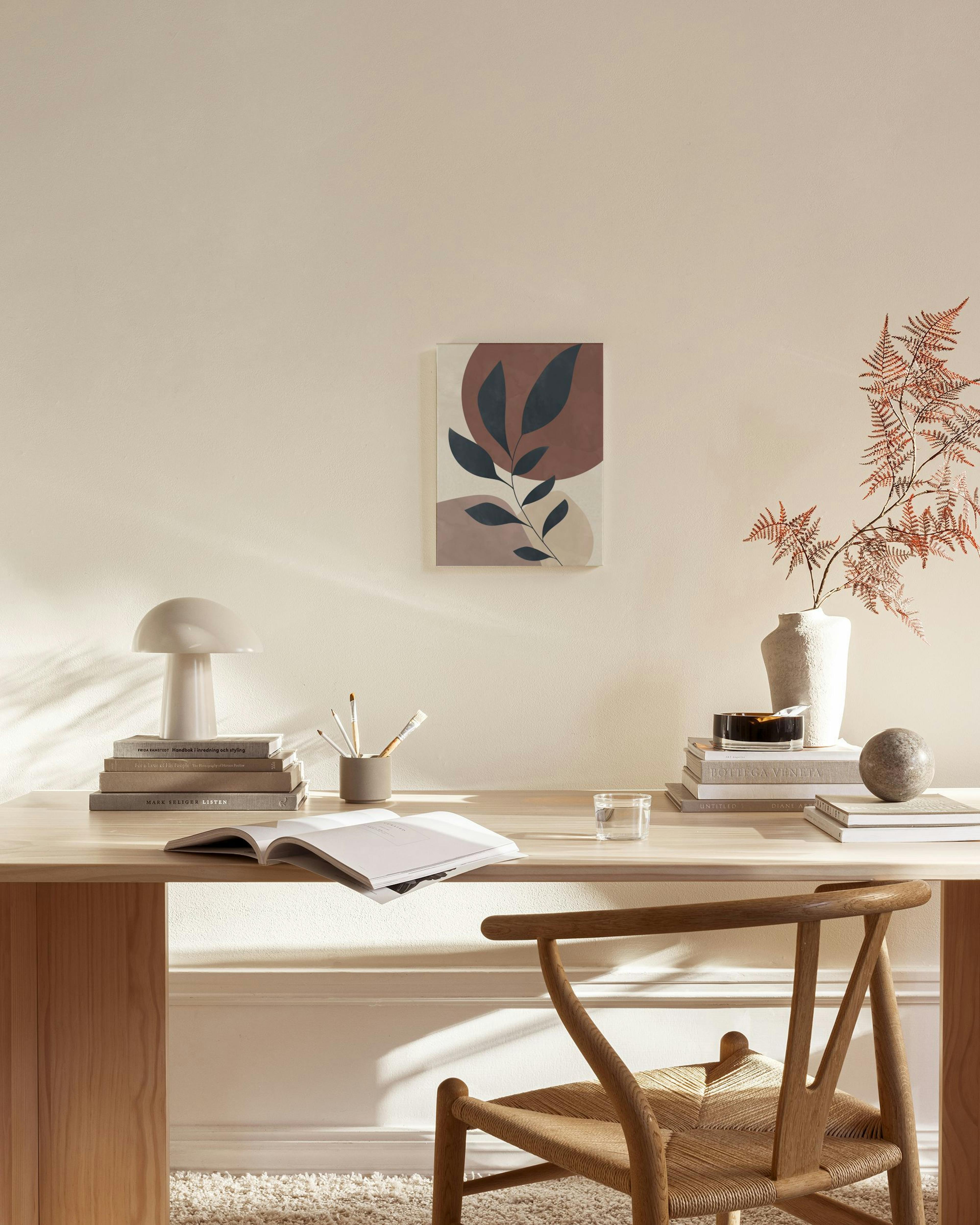 Botanical print with dark leaves on abstract rust and beige shapes, hanging in a minimalist living room.