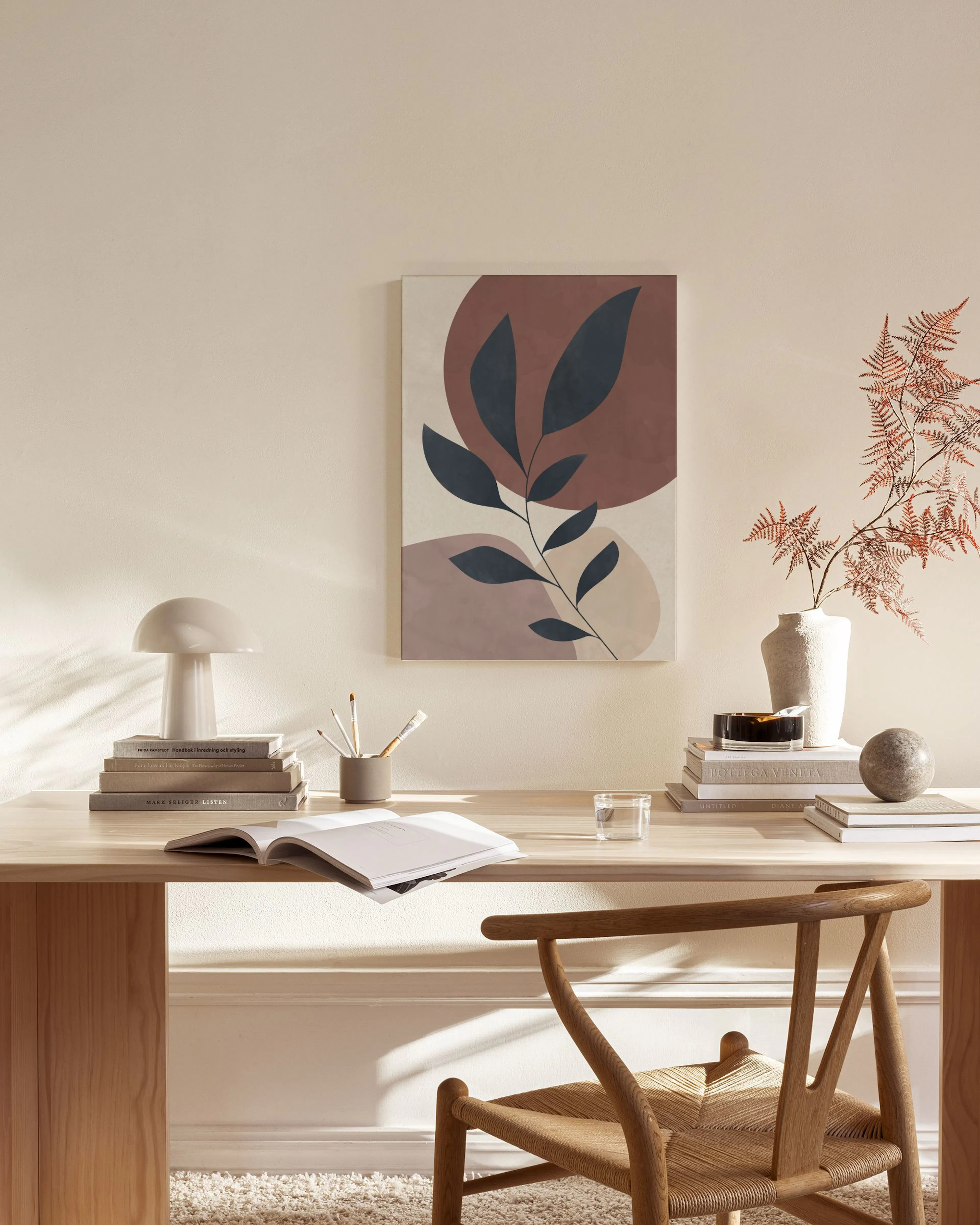 Abstract botanical canvas with dark leaves on terracotta and beige shapes, hanging in a bright living room.