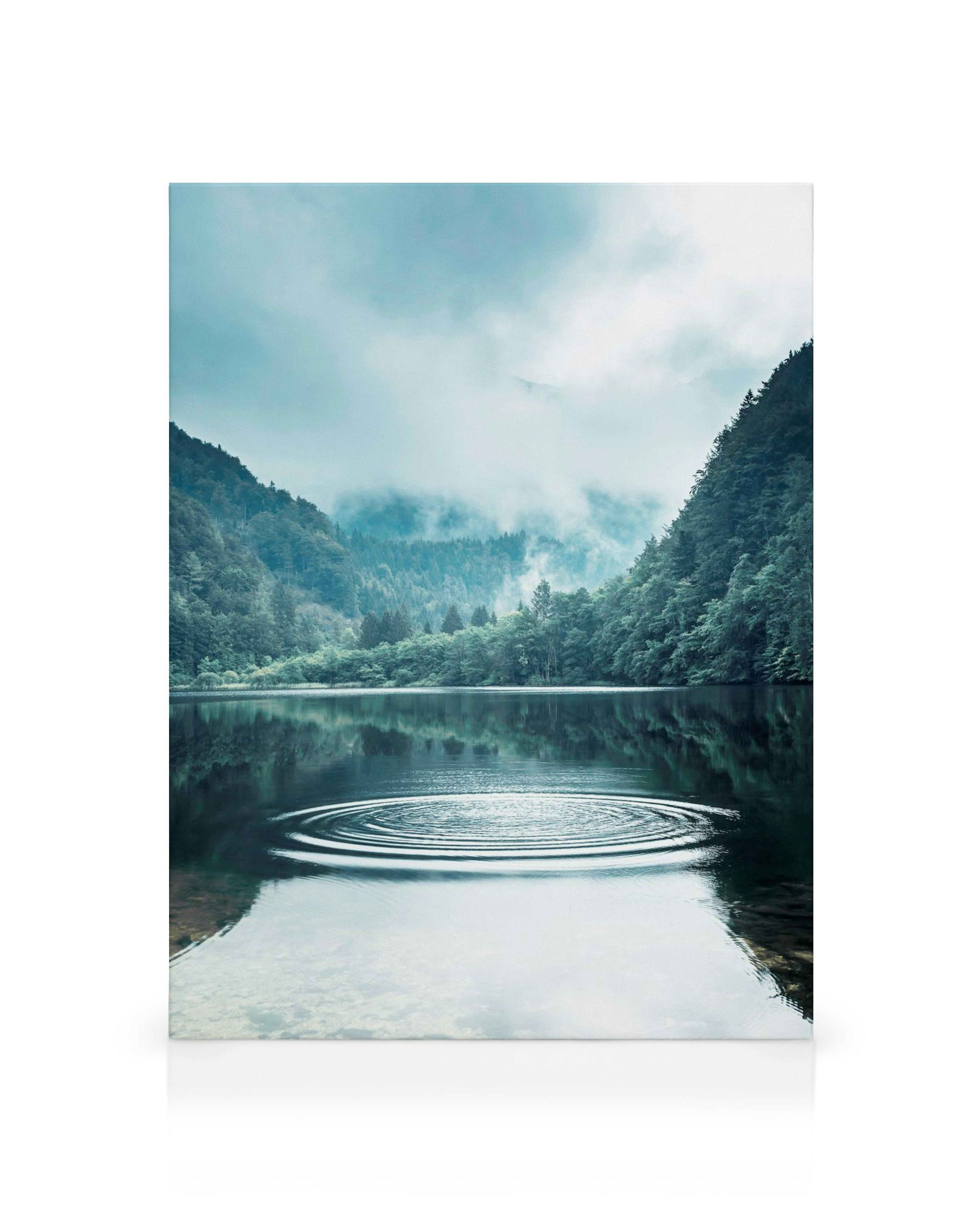 Tranquil landscape canvas print of a misty lake with concentric ripples, reflecting trees and hills in cool blues and greens.