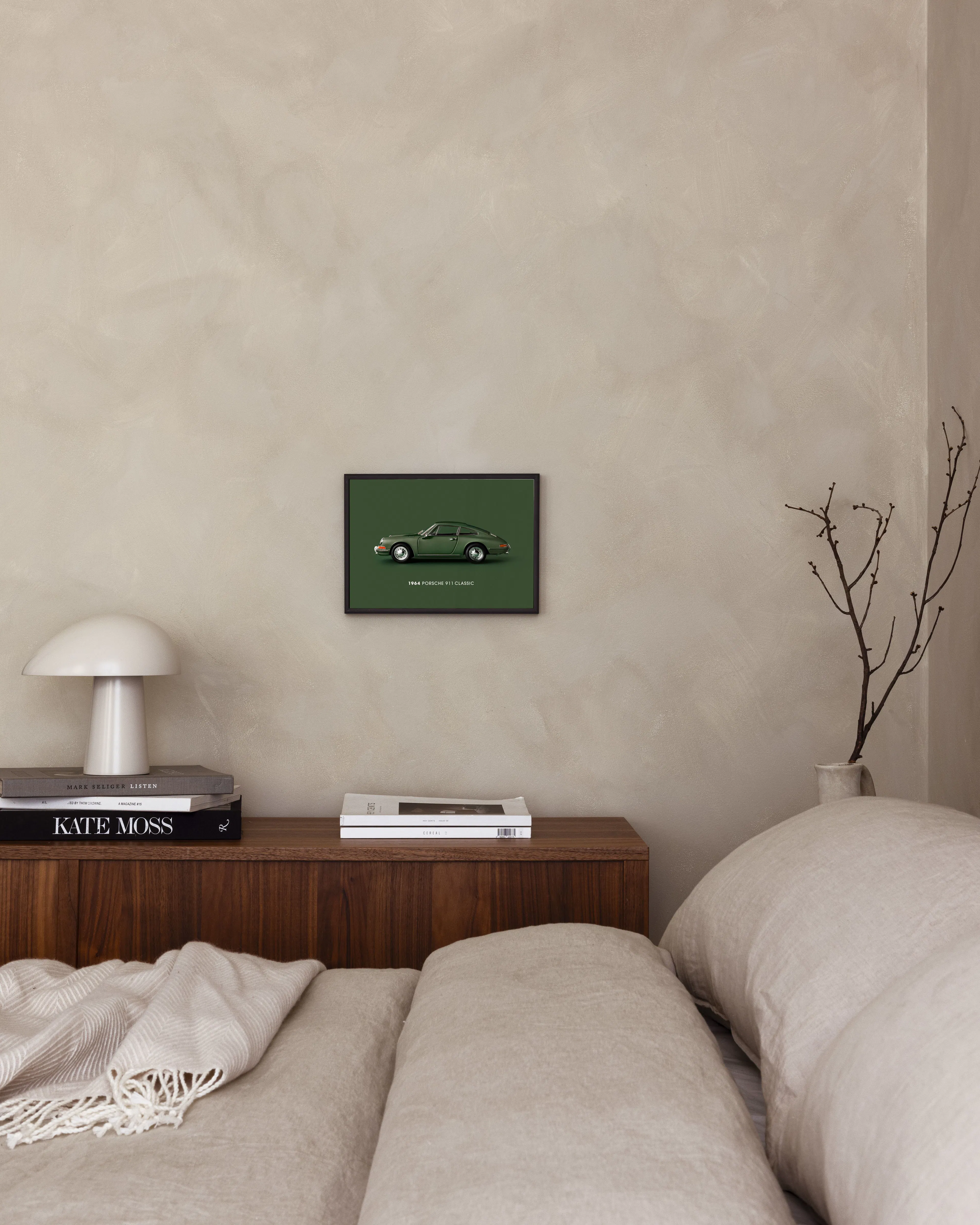 Poster med grön Porsche 911 Classic 1964, hänger i ett sovrum ovanför ett sängbord med lampa och böcker.