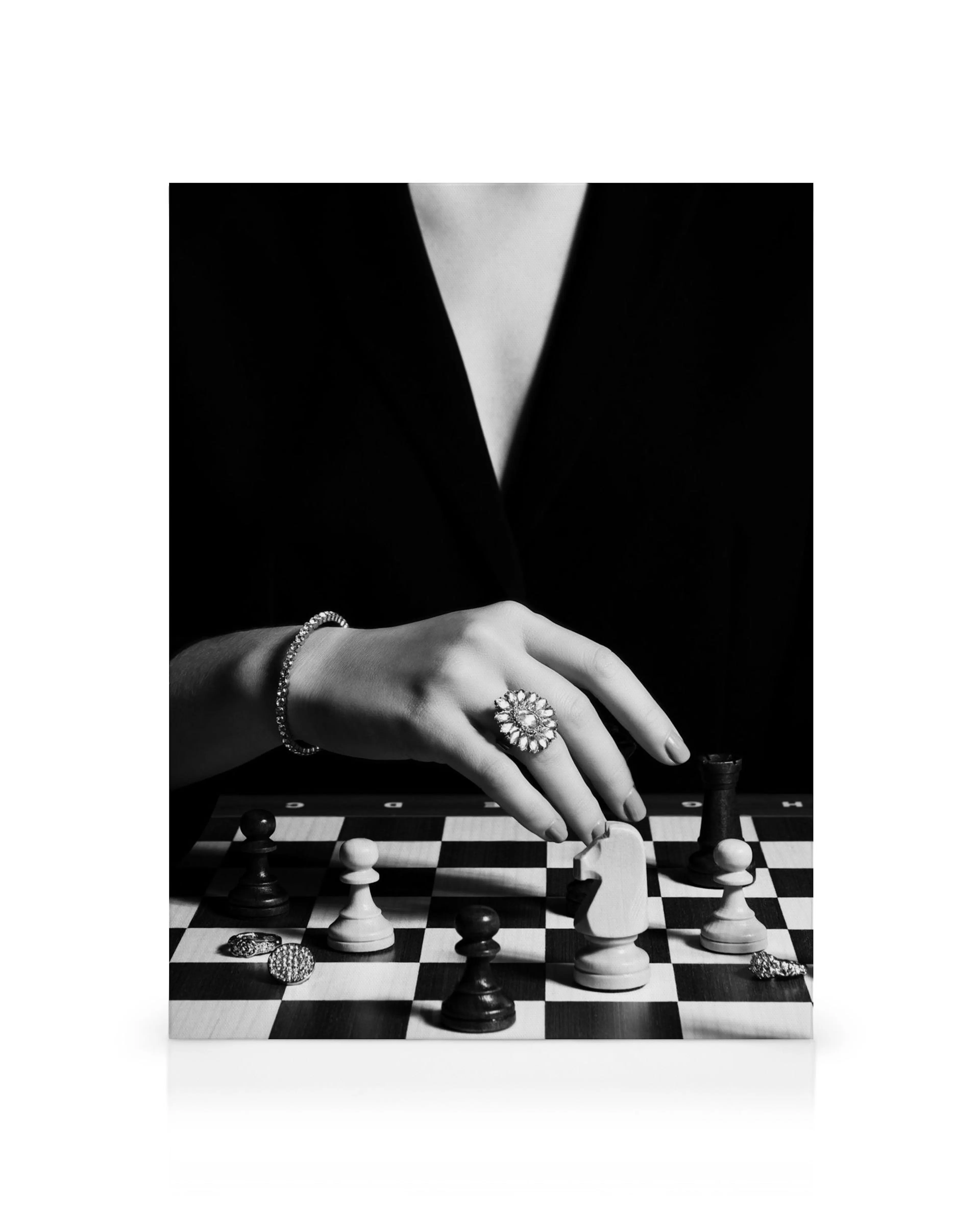 Black and white canvas print of a hand moving a knight chess piece on a chessboard, with a blurred figure in the background.