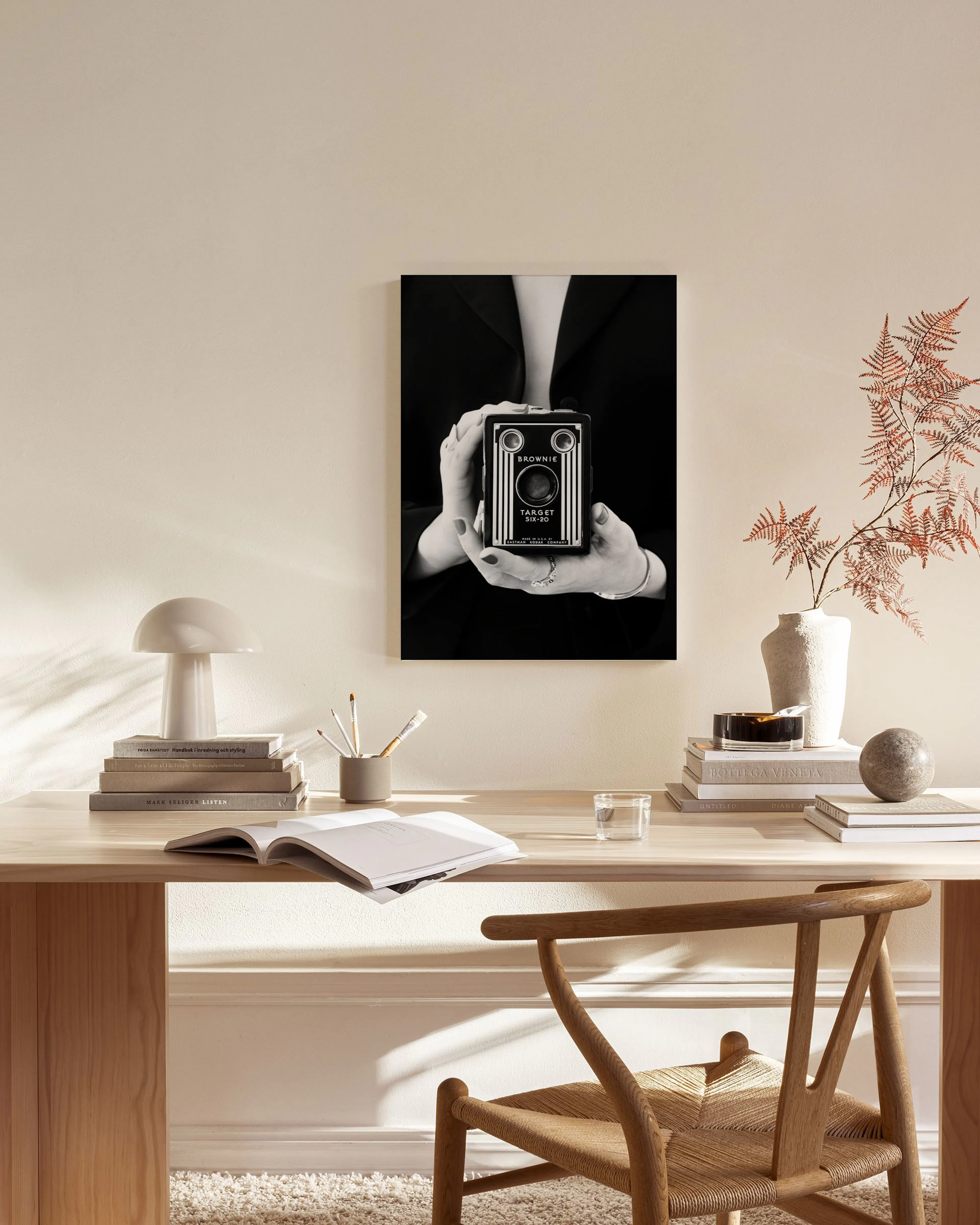 Toile noir et blanc dune femme tenant un appareil photo vintage, suspendue dans un salon beige avec une table basse en verre.