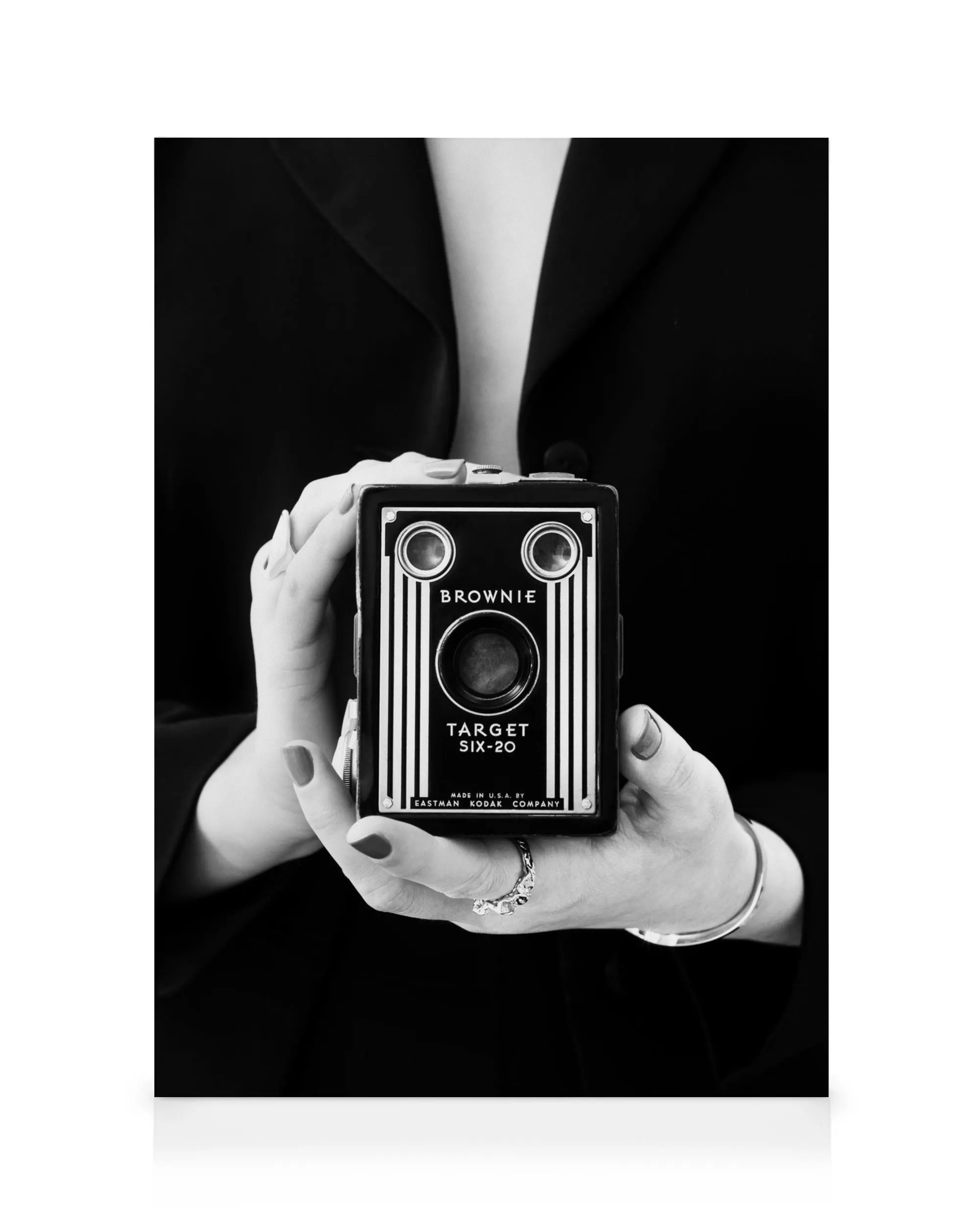 Mãos segurando uma câmera vintage preta e prata Brownie Target Six-20 em fundo escuro, fotografia monocromática.