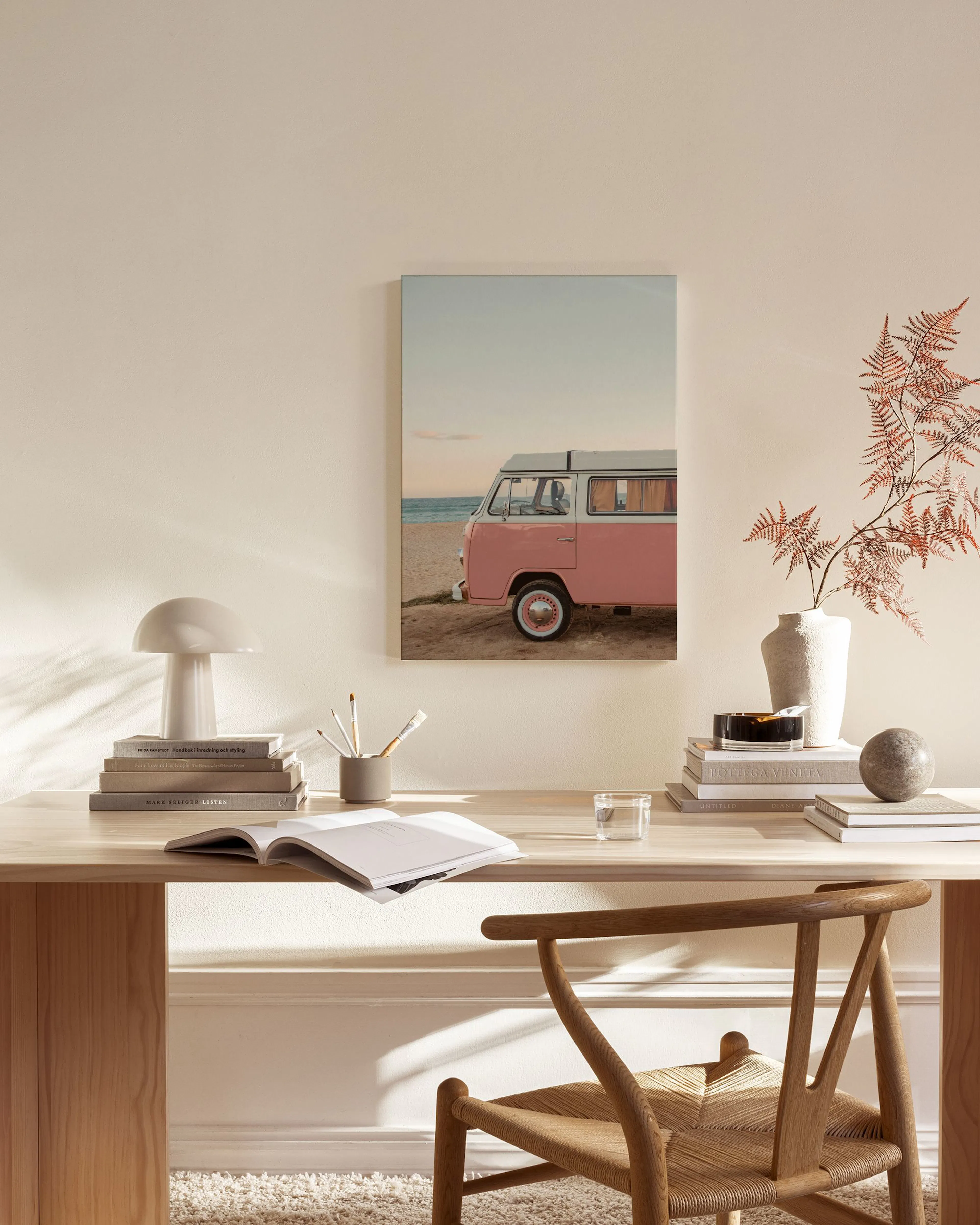 Lienzo de una furgoneta rosa estacionada en la playa, colgado en una sala de estar moderna con muebles de madera.