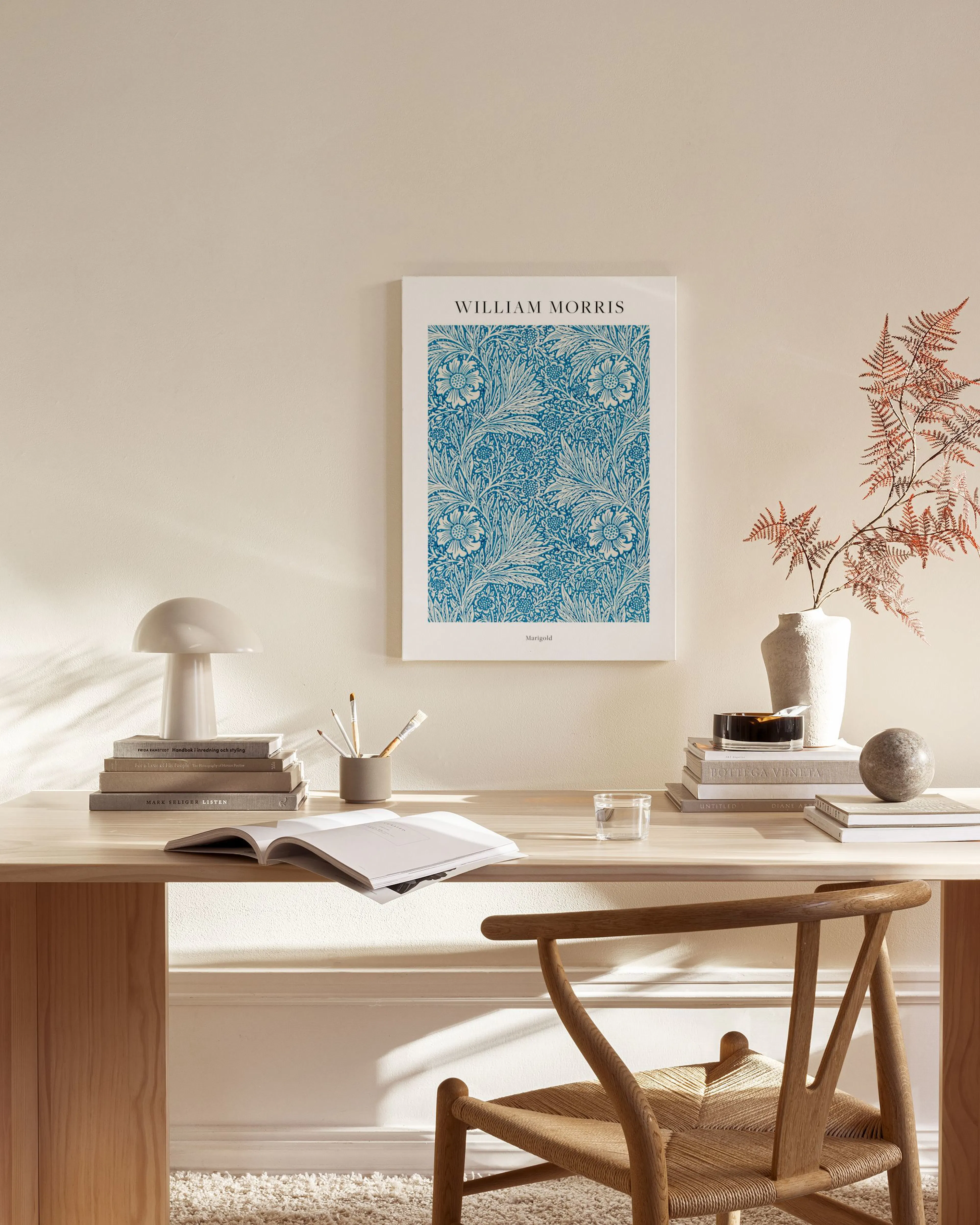 Stampa su tela William Morris con motivi floreali blu, appesa in un soggiorno moderno sopra un mobile basso in legno.