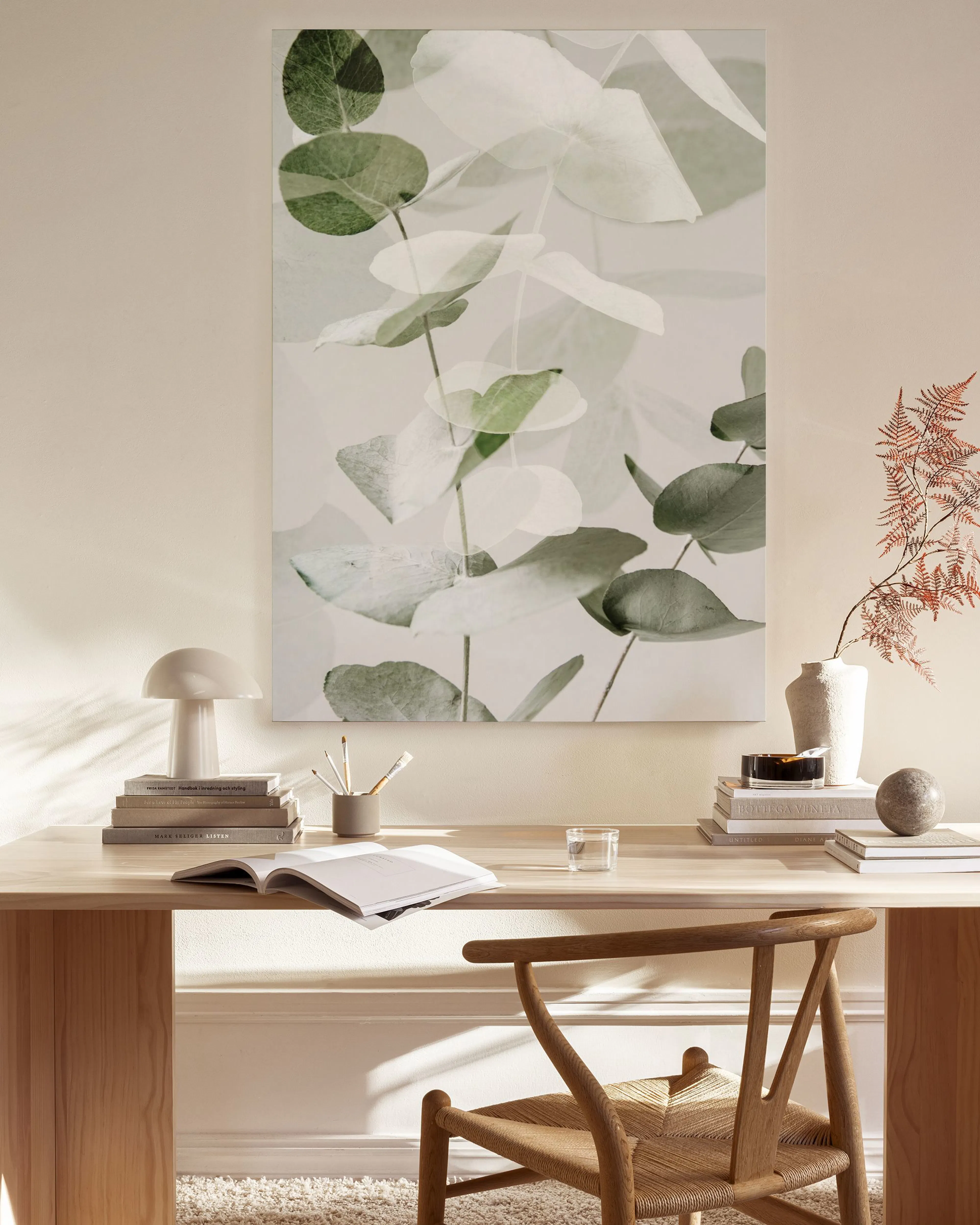 Botanical canvas print of eucalyptus leaves in muted greens and whites, hanging above a wooden console in a minimalist living ro