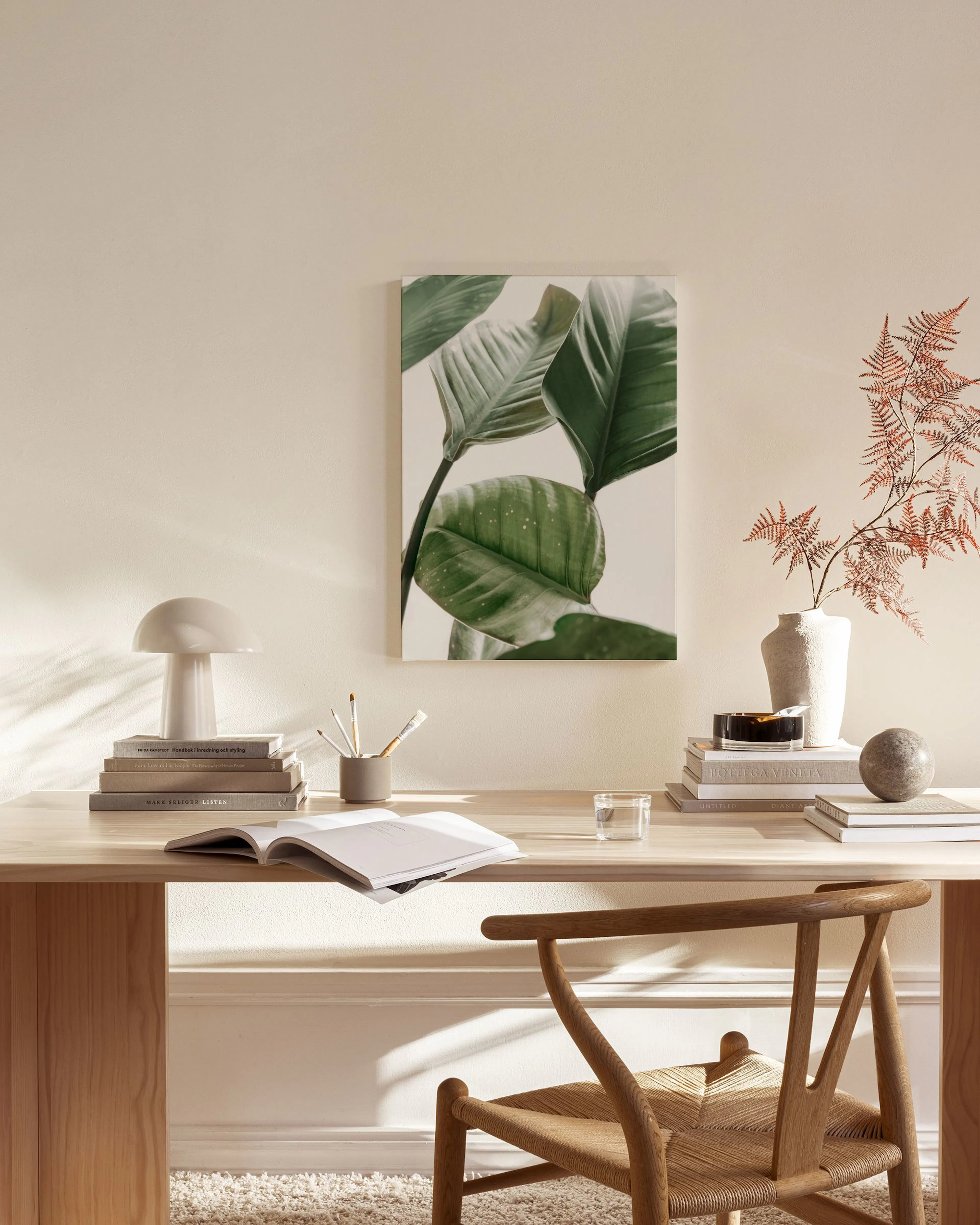 Canvas print of large green tropical plant leaves, displayed above a wooden console table in a minimalist living room.