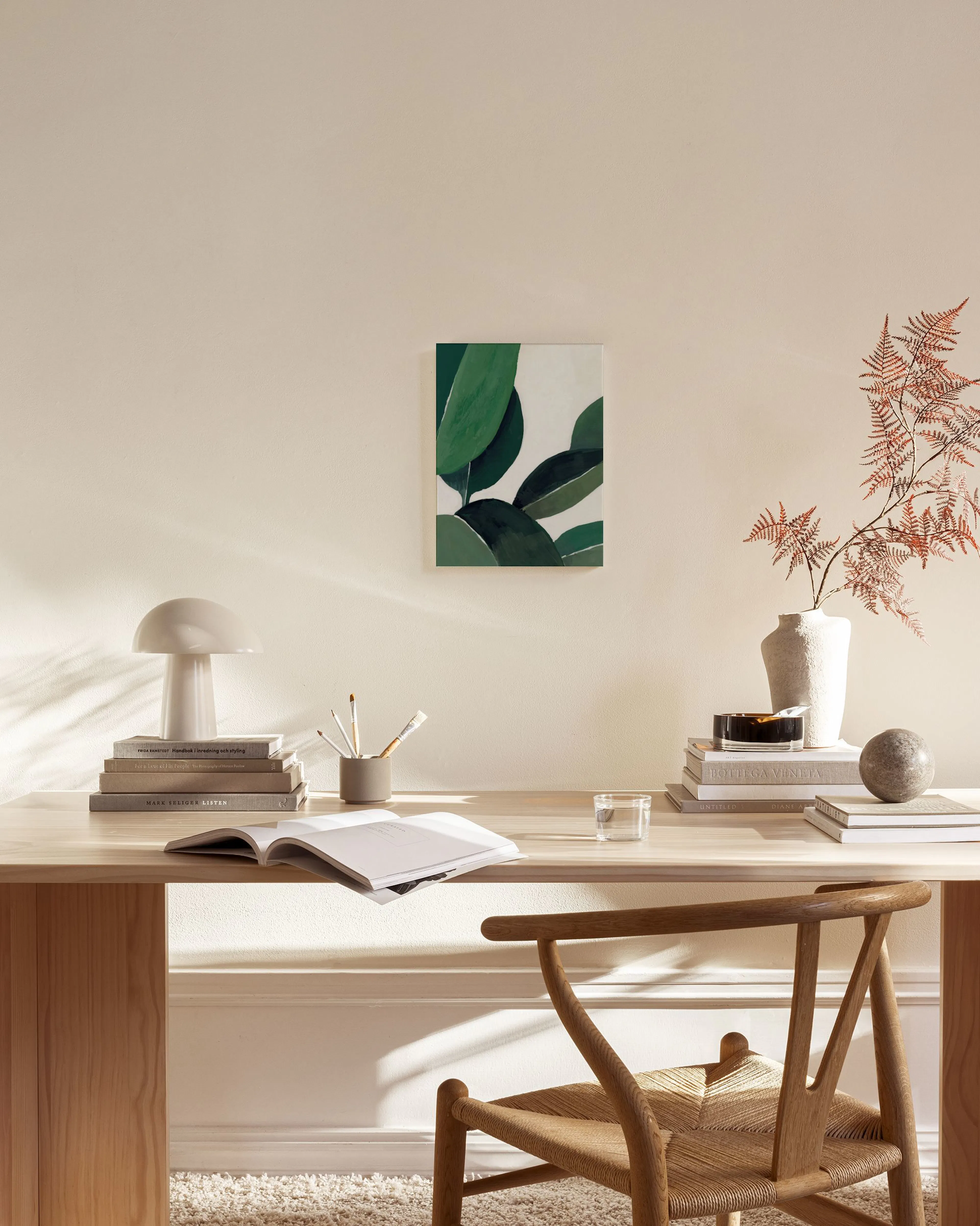 A canvas print featuring lush green leaves on a white background, displayed in a bright, minimalist living room above a wooden c