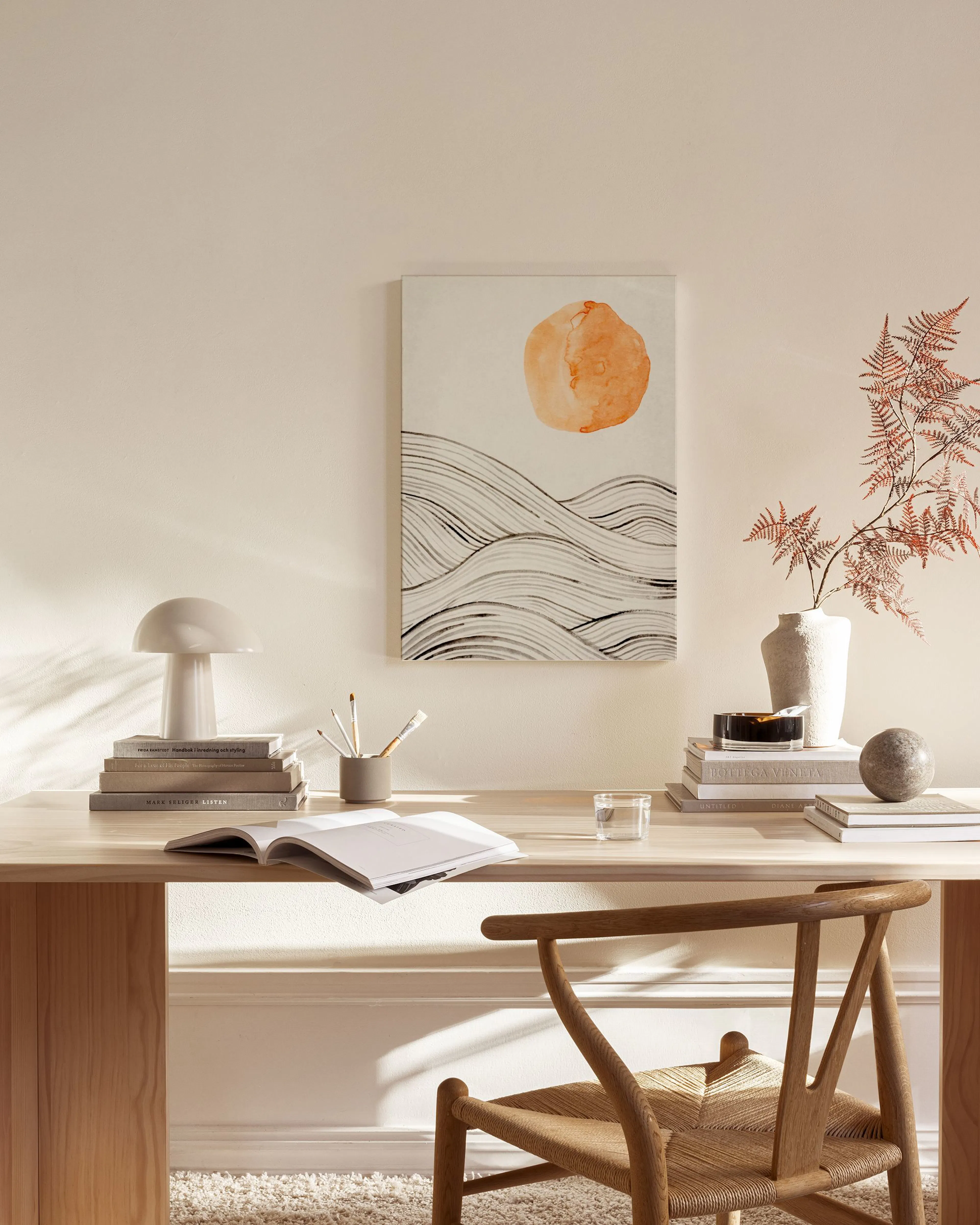 A canvas print of an orange sun over black abstract waves, displayed in a modern living room above a wooden console table.