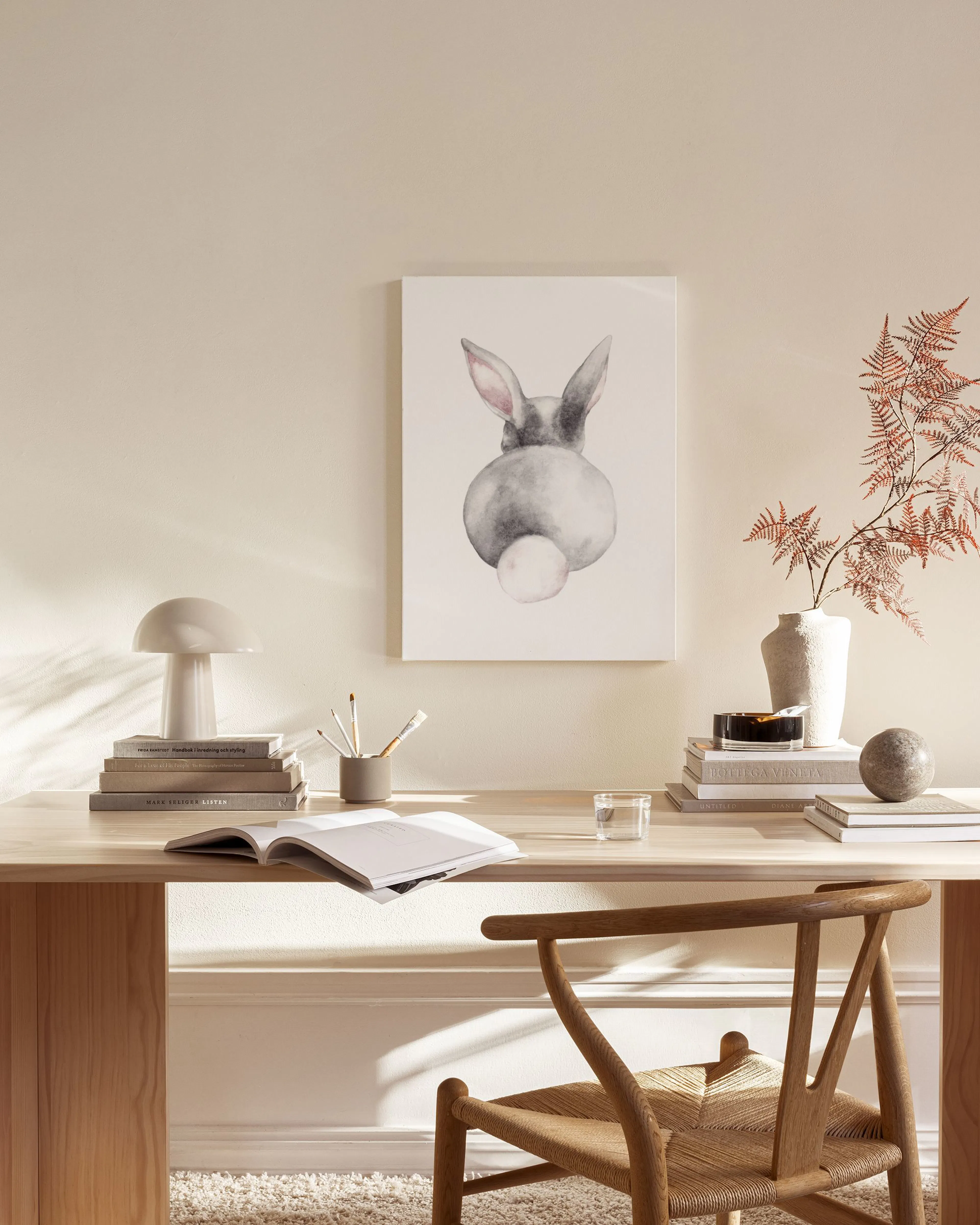 Leinwandbild eines süßen Hasen von hinten mit rosa Schwänzchen, hängt über einem Holzregal in einem hellen Wohnzimmer.