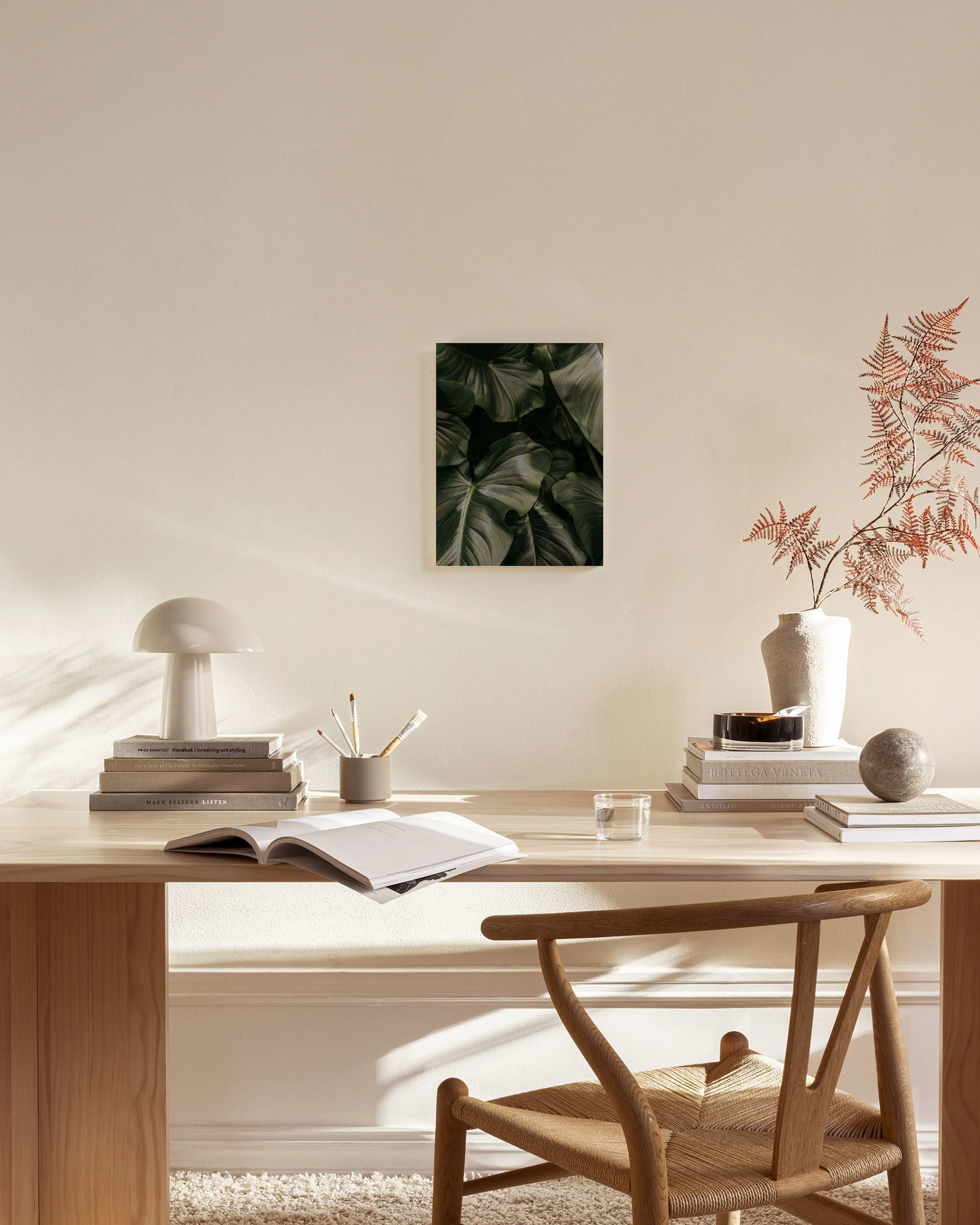 Toile murale de feuilles tropicales vert foncé, suspendue dans un salon scandinave clair au-dessus dun banc en bois.
