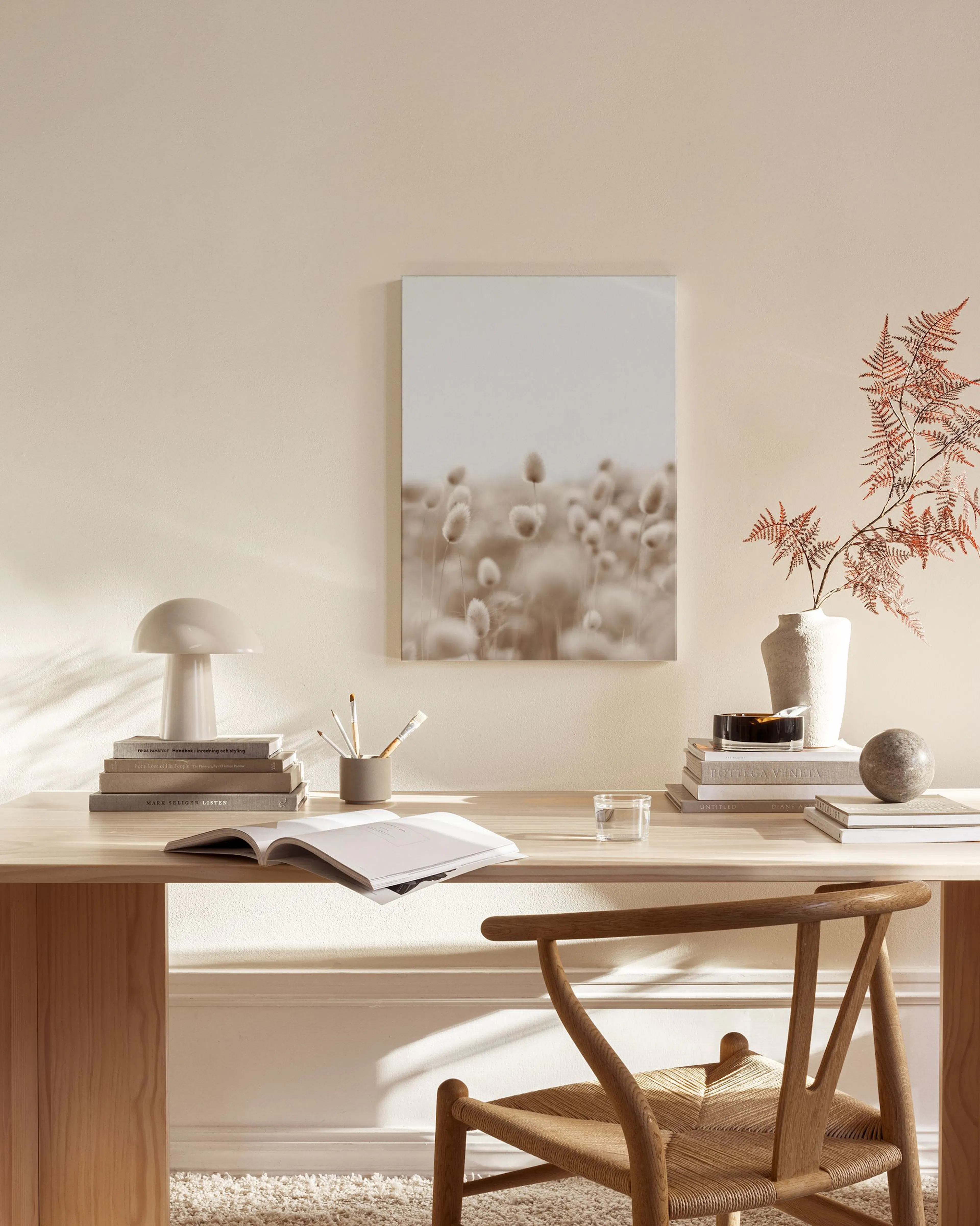 Canvas met een veld van pluizige, bruine plantjes tegen een lichte lucht, hangend in een neutrale woonkamer.