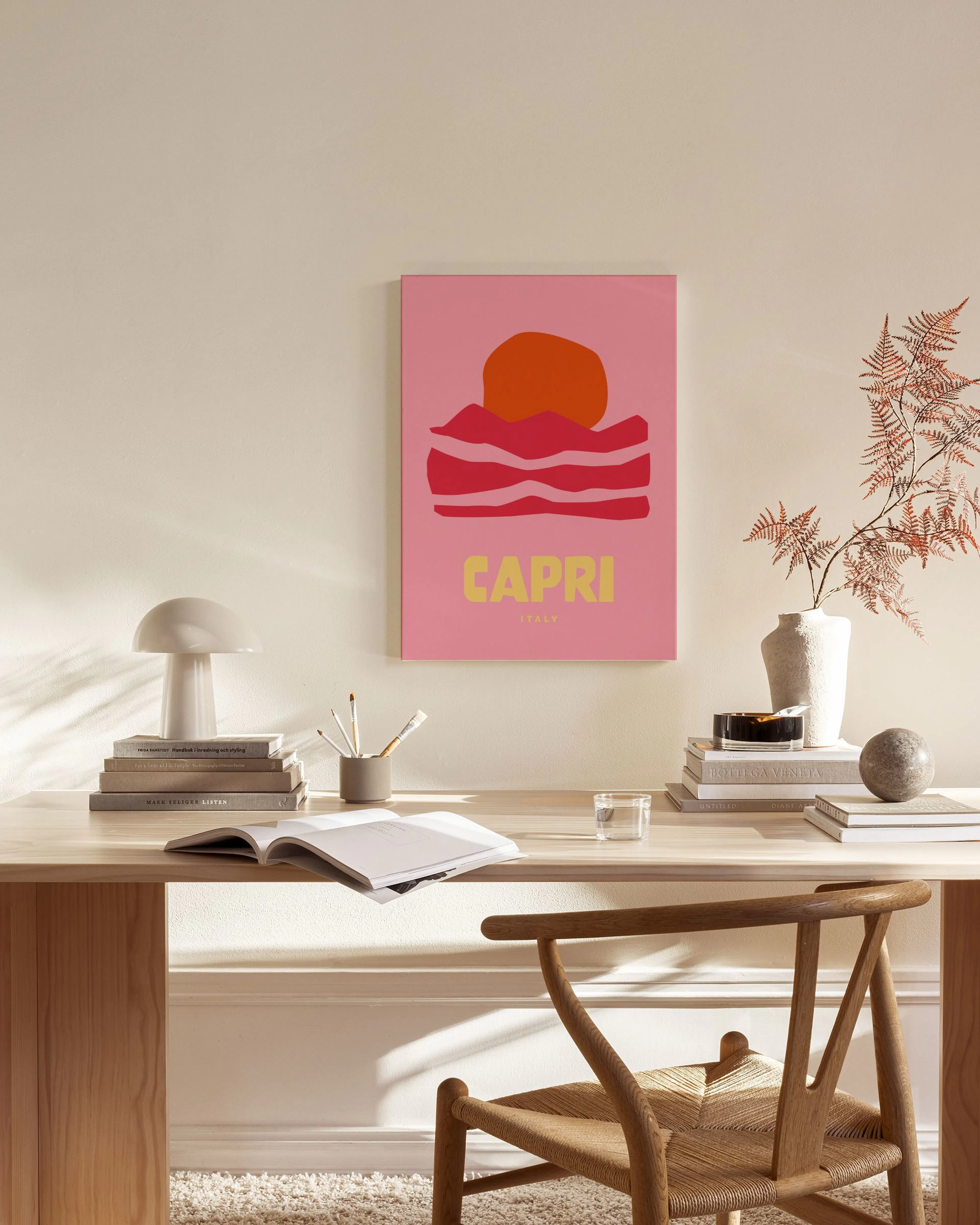 Leinwandbild mit rosa Hintergrund, oranger Sonne, roten Wellen und dem Schriftzug CAPRI ITALY, hängend in einem stilvollen Wohnz