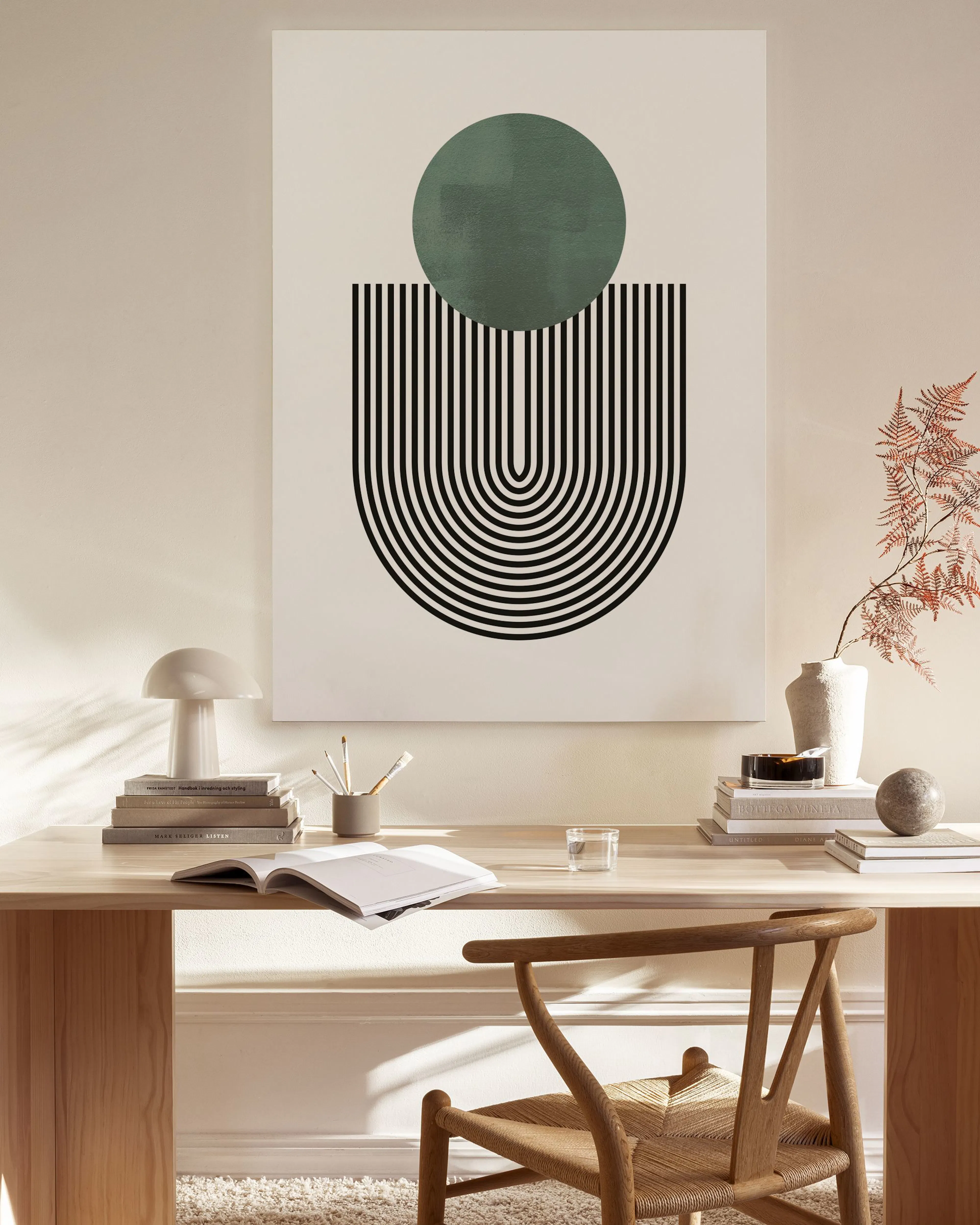 A canvas print with a green circle above black and white concentric arches, hanging in a light-filled living room.