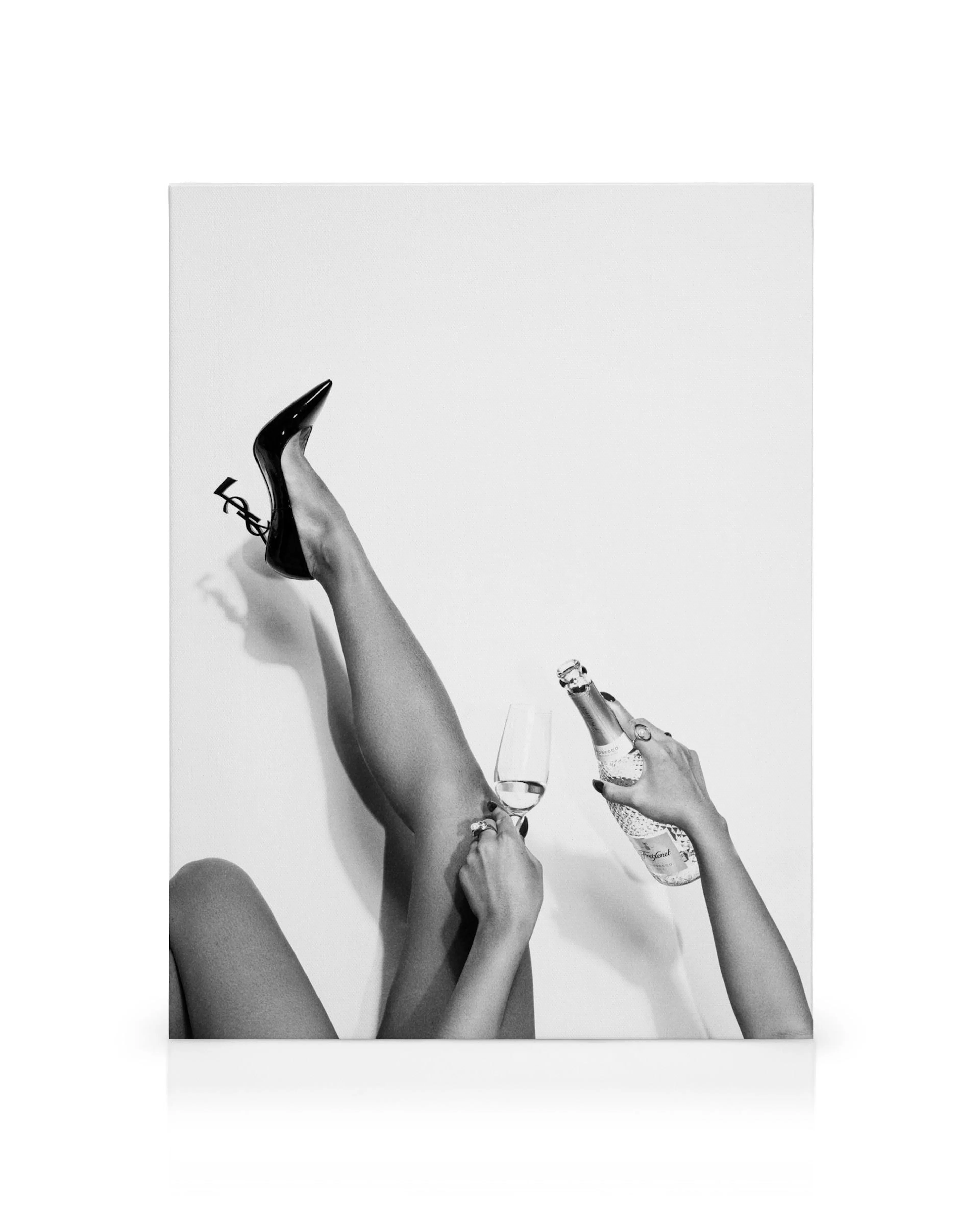 Tela de pernas cruzadas em preto e branco com salto alto YSL, taça e garrafa de champanhe, fotografia elegante.