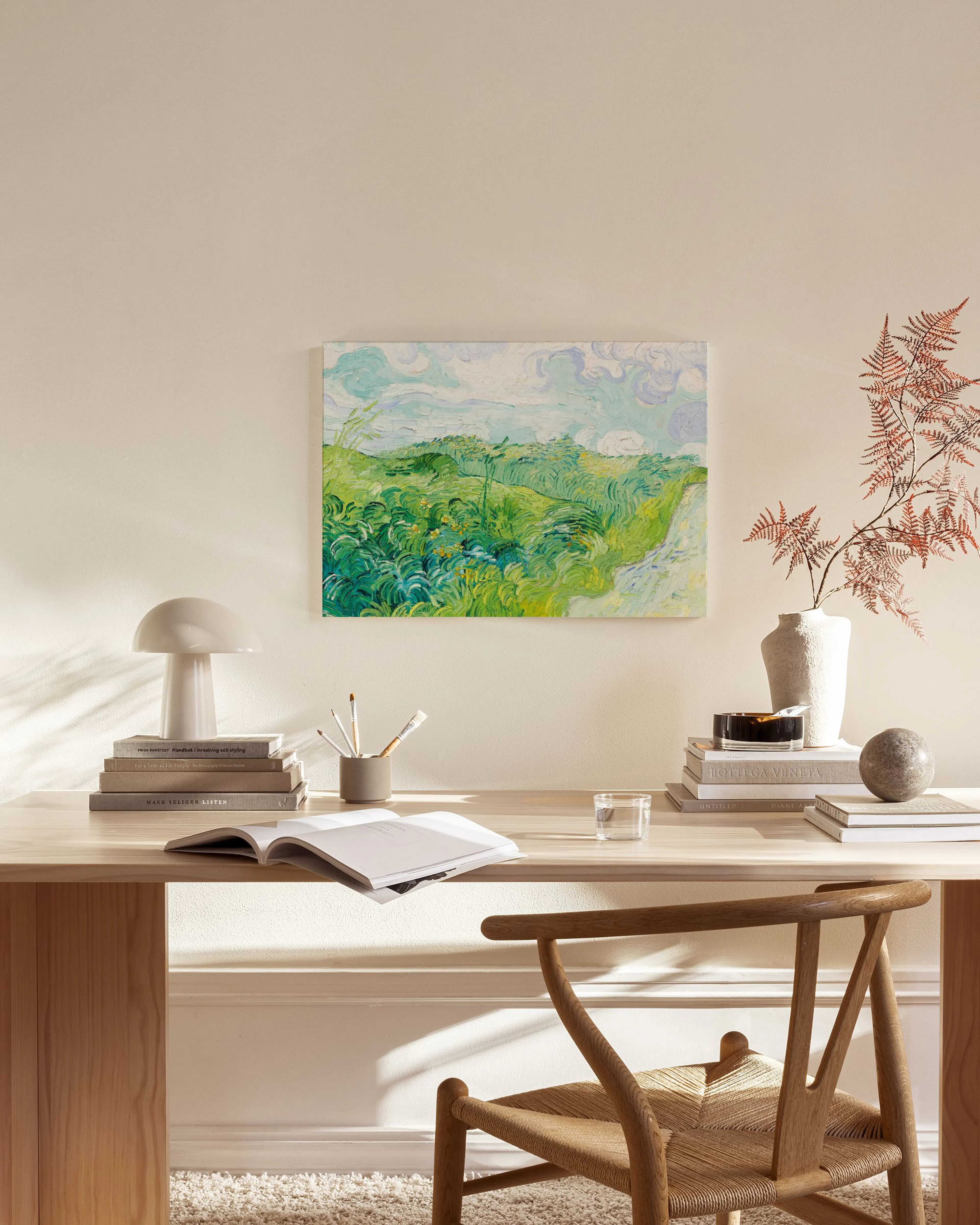 Impressionistic landscape canvas print with green fields and a light blue sky, hanging above a wooden console in a bright living
