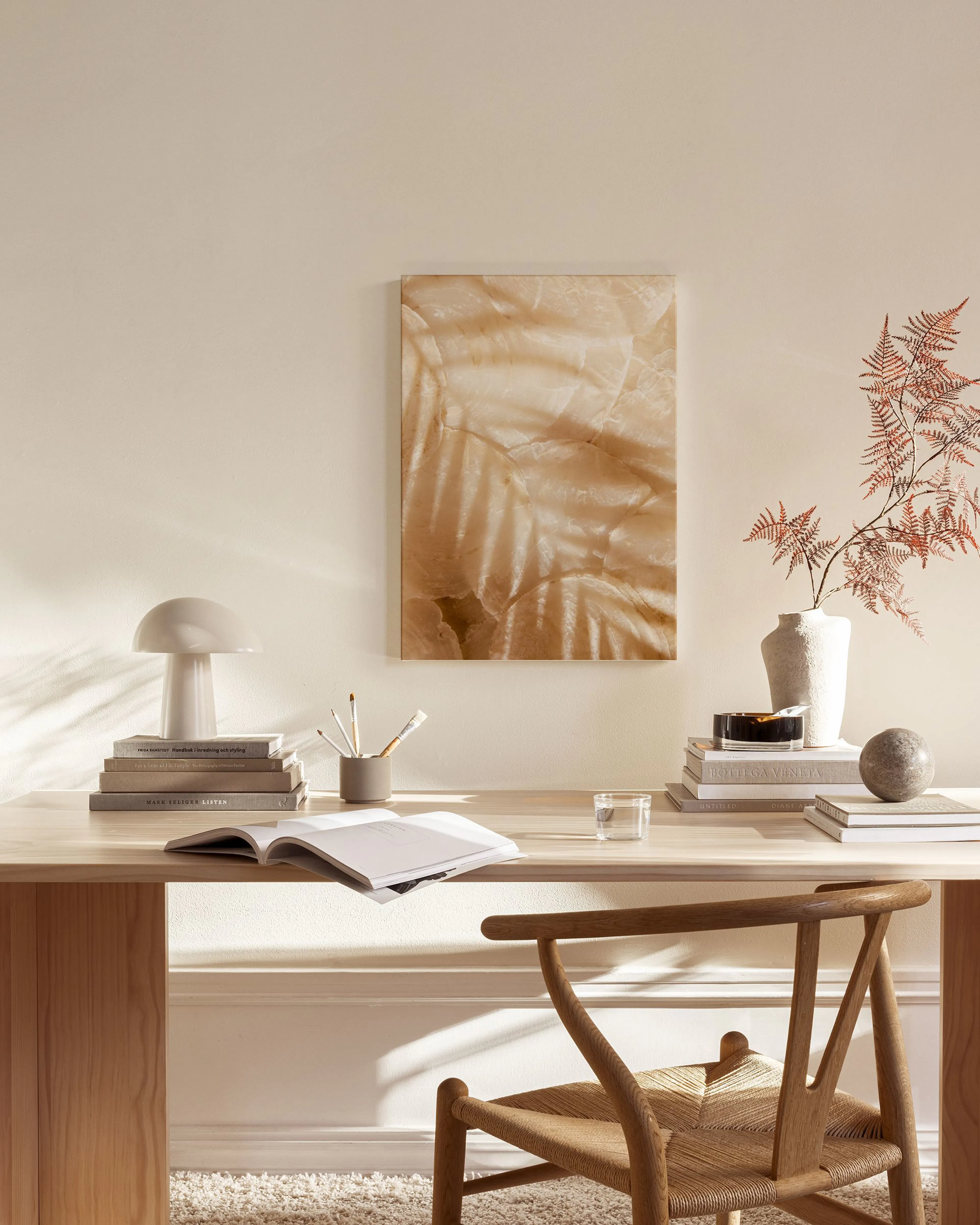 A canvas print of translucent palm leaves in warm beige and brown tones, hanging in a neutral-toned living room.