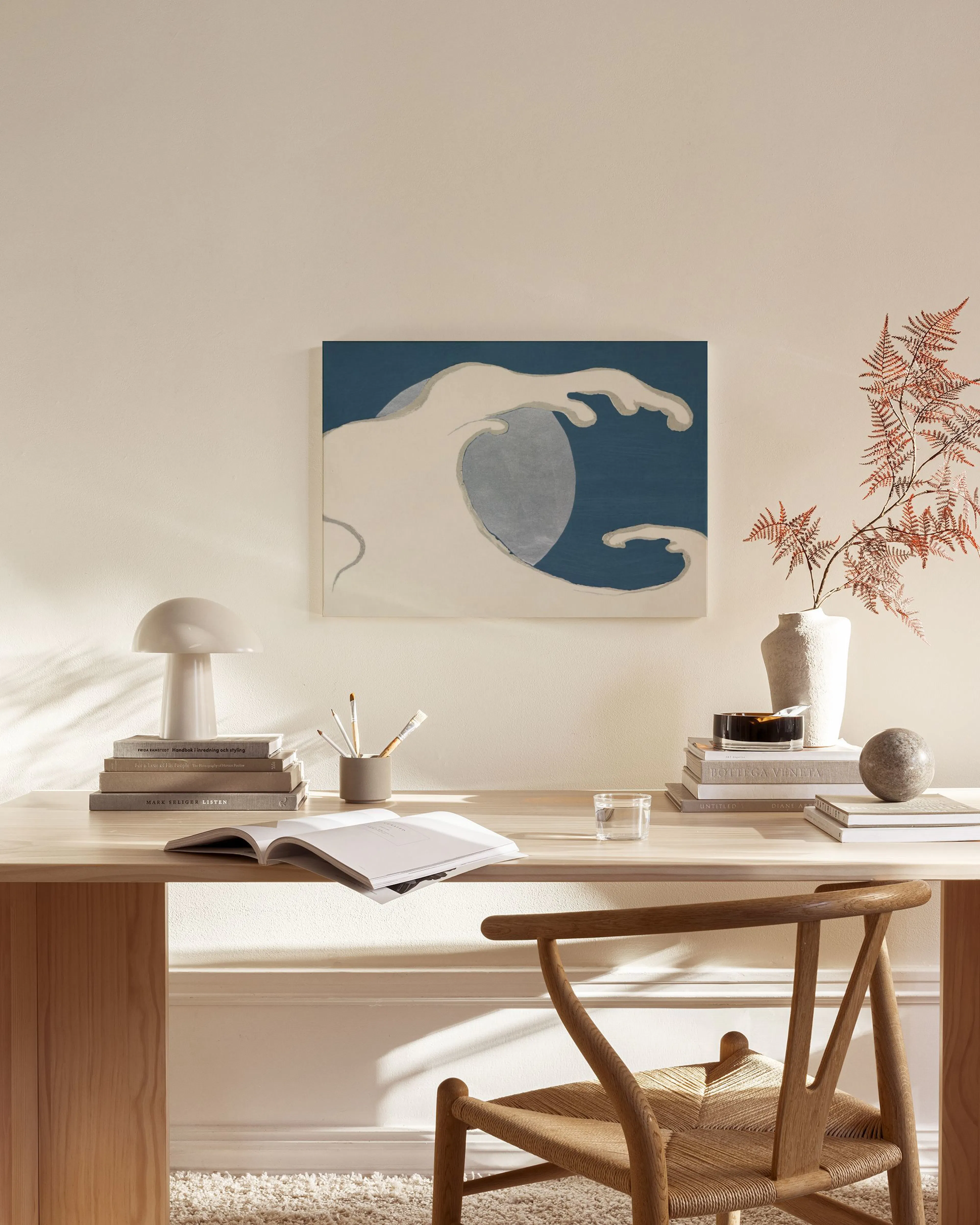 A canvas print of a white and grey abstract wave on a dark blue background, hanging in a minimalist living room.